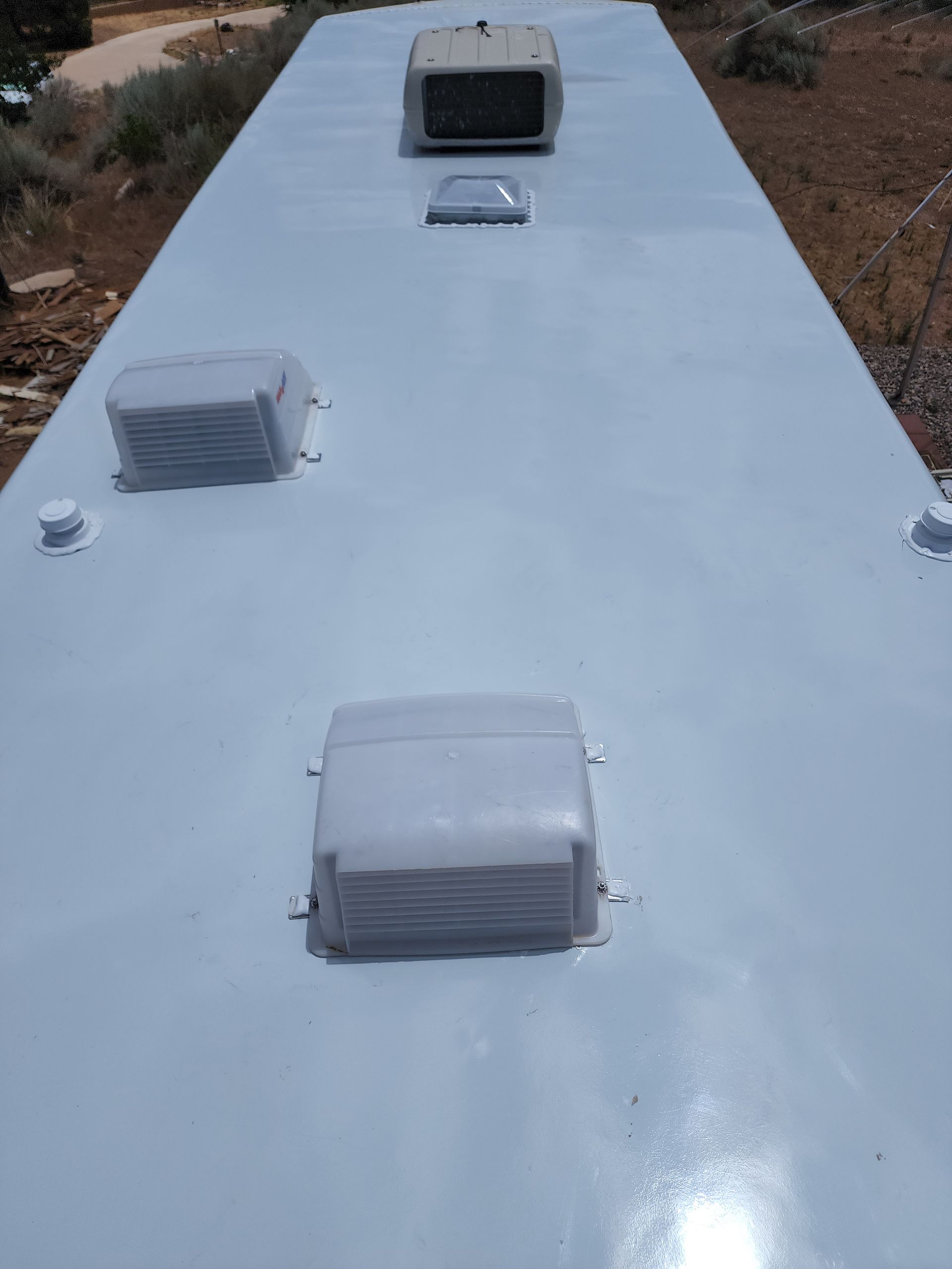 Light blue RV roof with air vents and antenna on a sunny day.