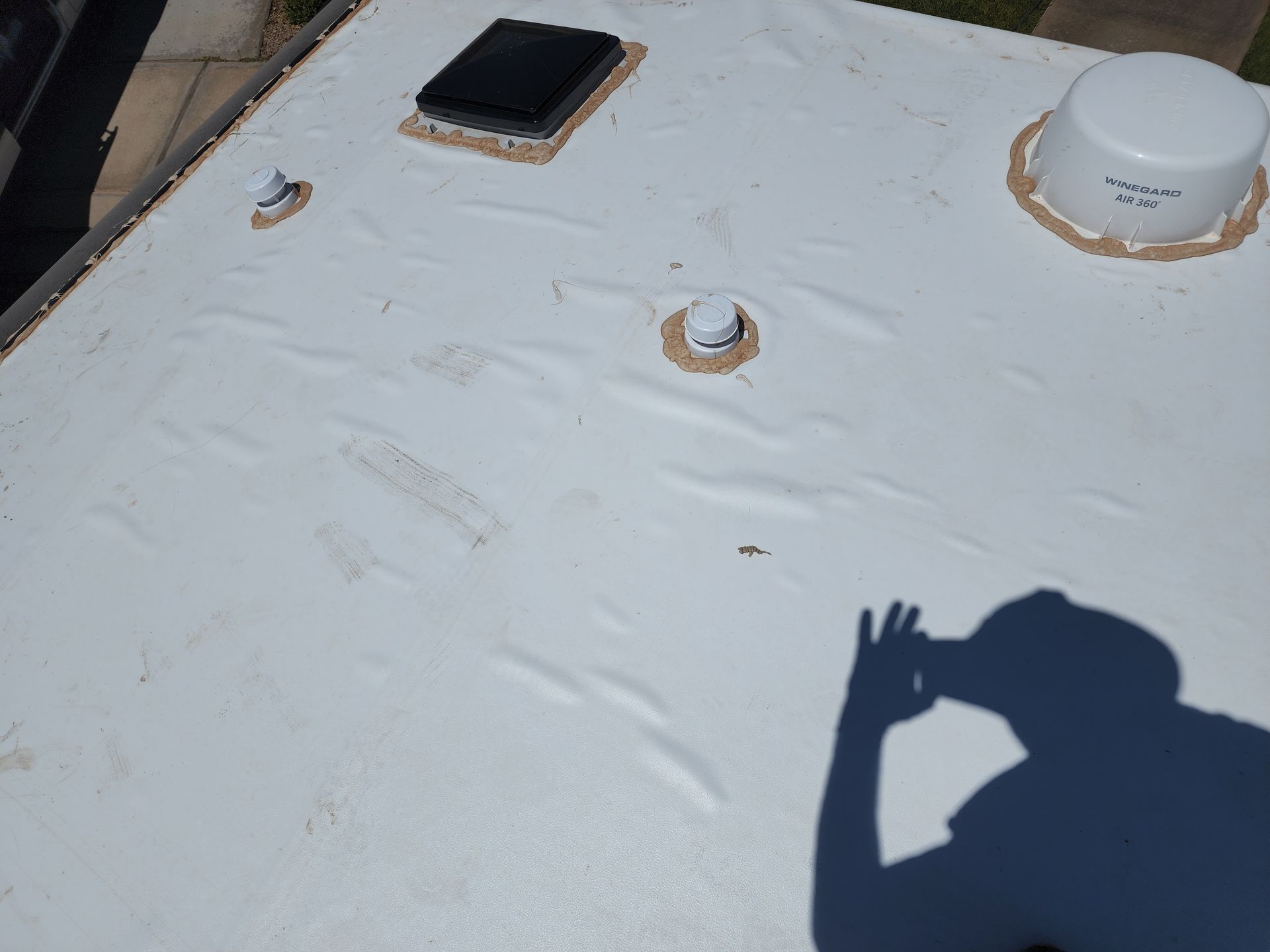 White RV roof with vents and satellite dish; shadow of a person taking a photo.