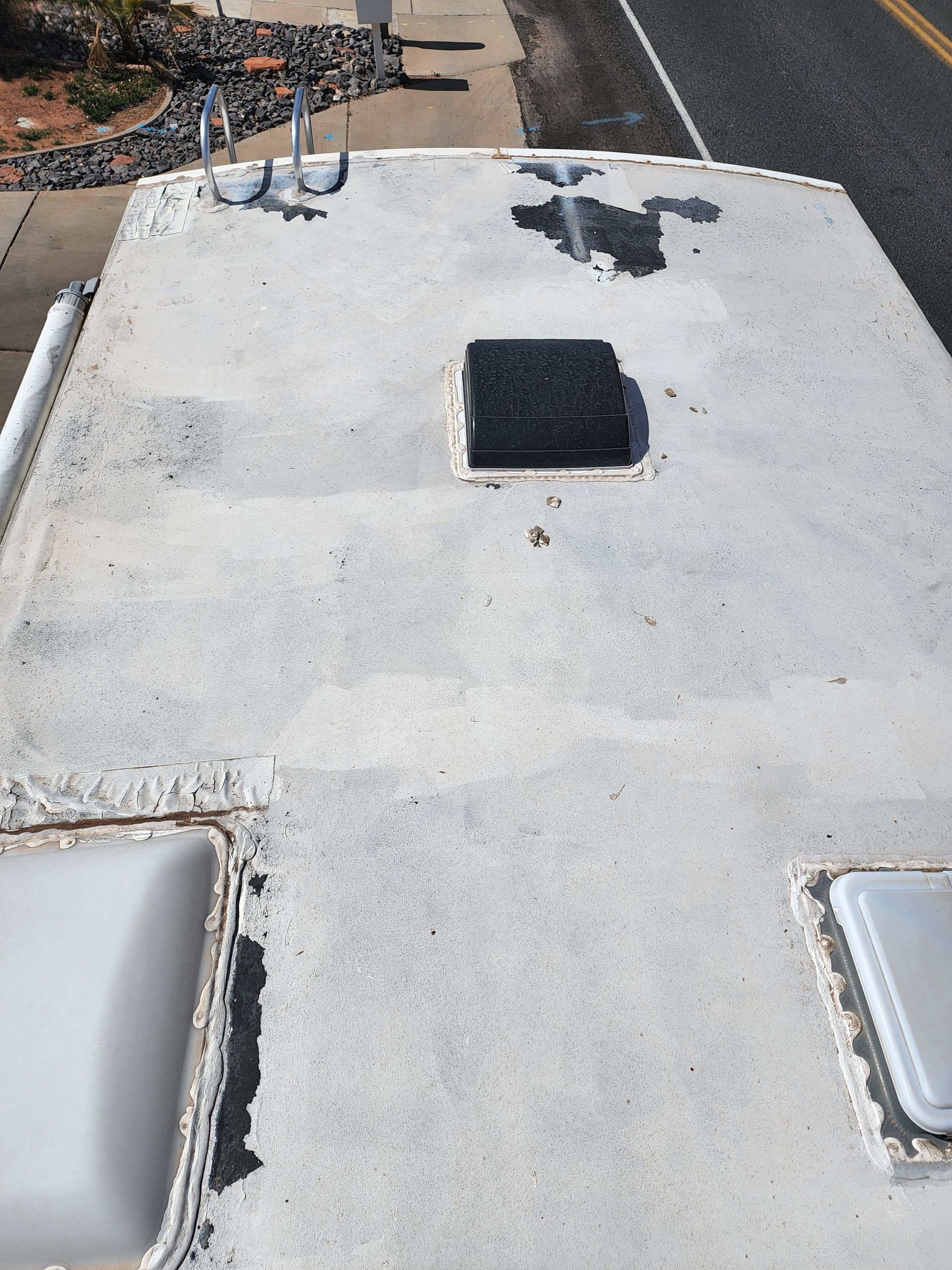 RV roof with damaged white coating and square opening.