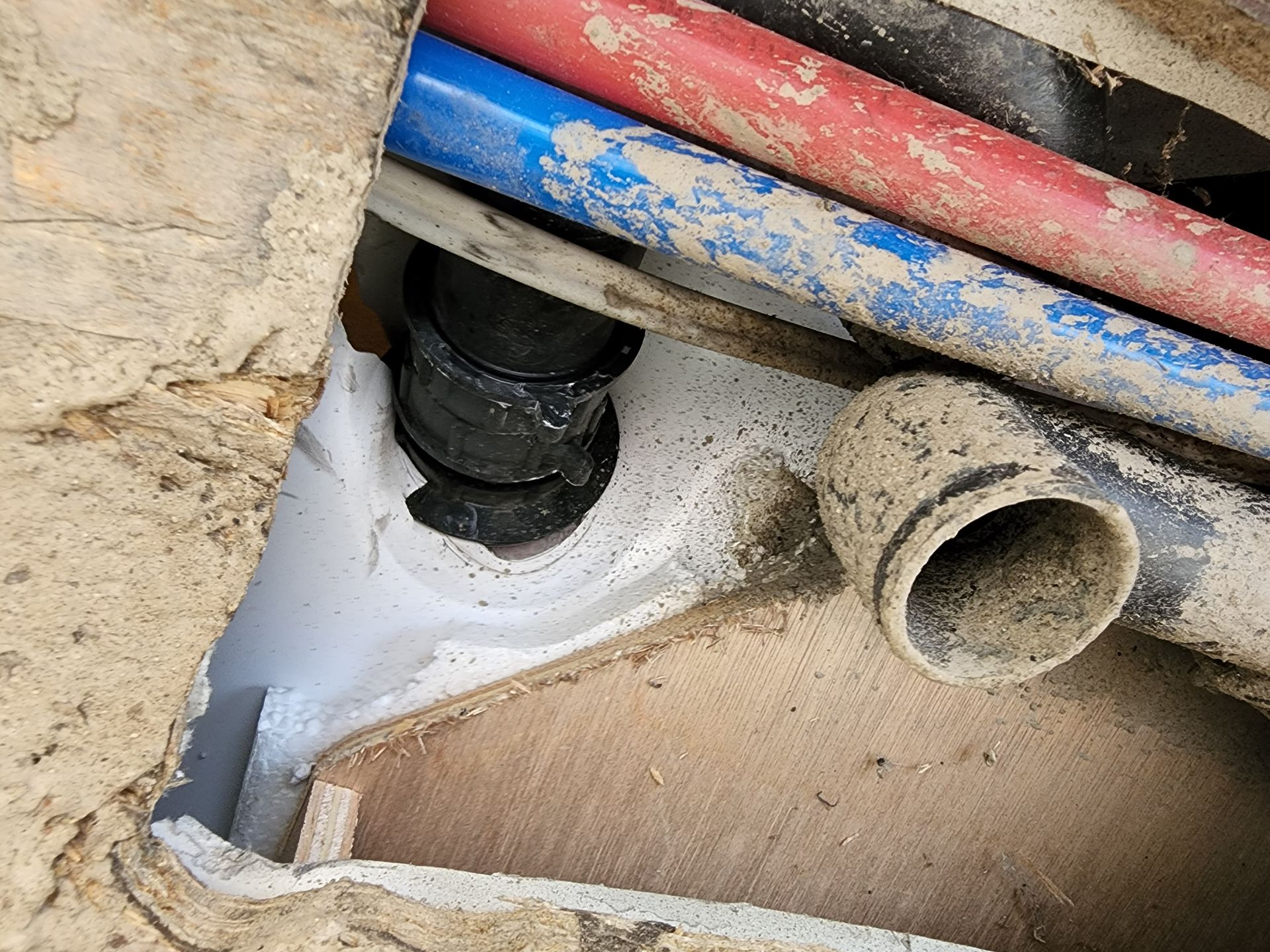 Pipes of different colors and a black pipe joint are visible in a small concrete enclosure.