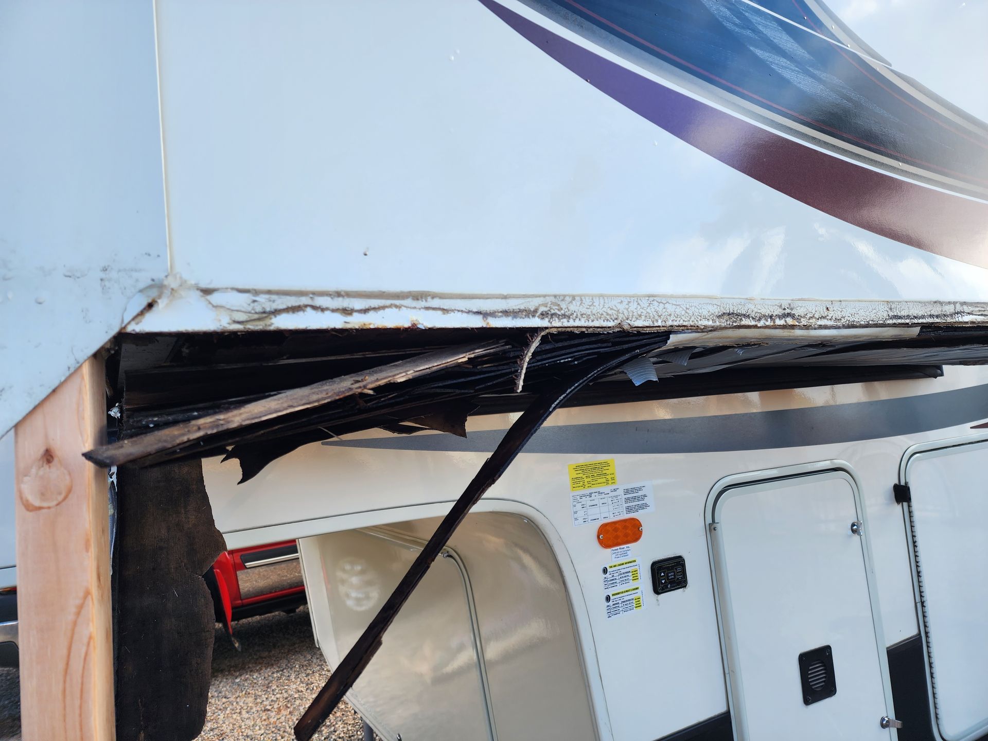 Damaged RV awning with ripped black fabric, white exterior, and a wooden support beam.