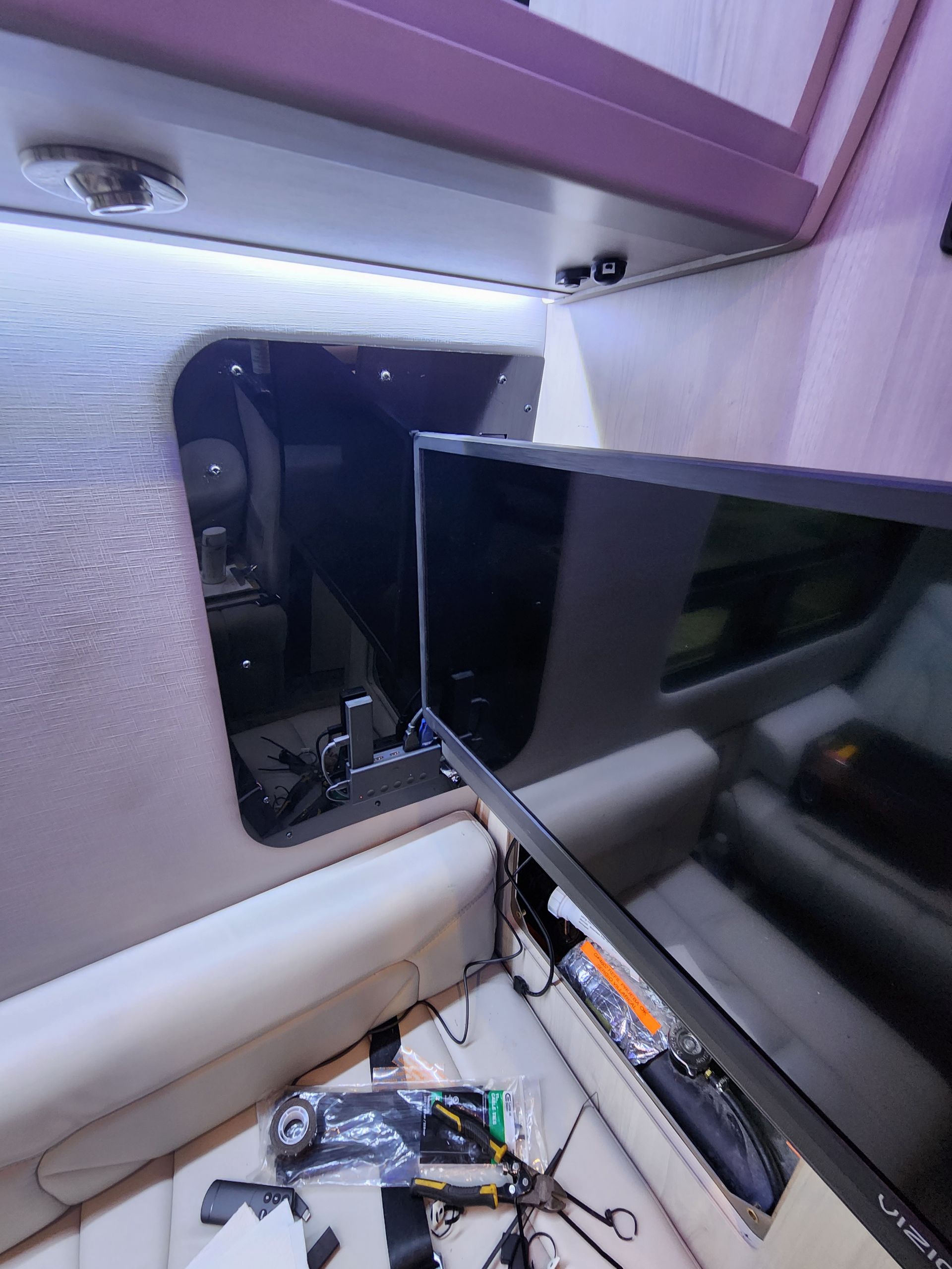 Interior of a van with a mounted TV and open compartment. Wires and remote control on the seat.