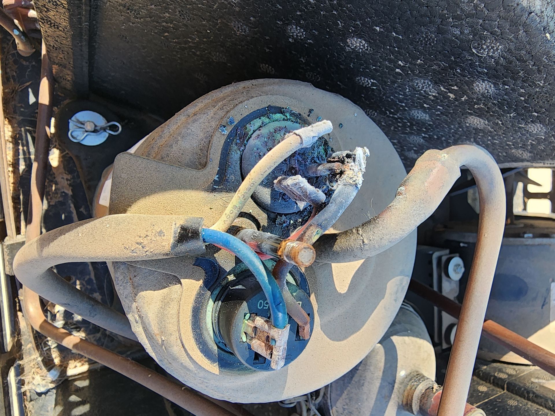 Damaged air conditioning compressor with exposed wires, covered in dust and debris.