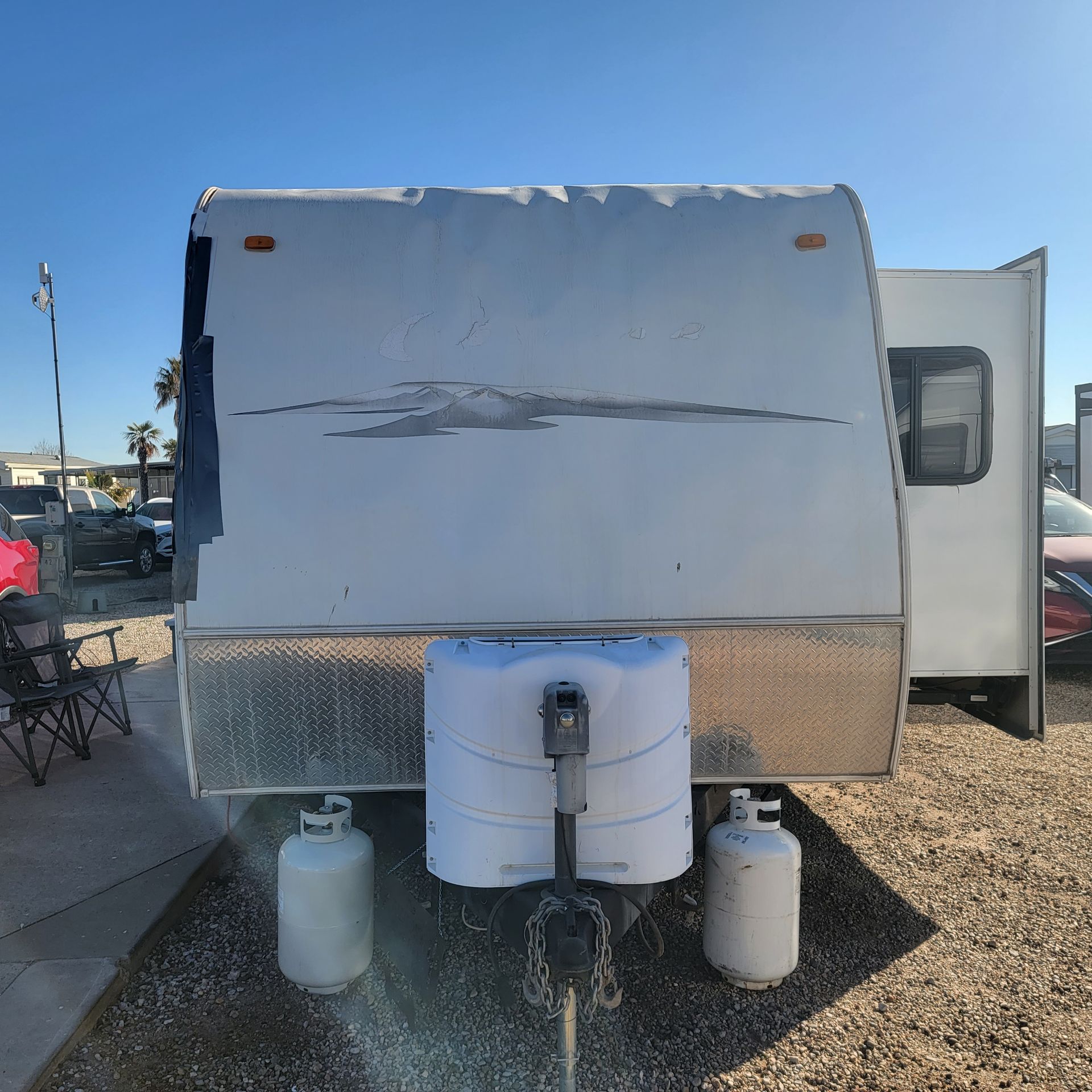 White travel trailer with propane tanks, parked outside.