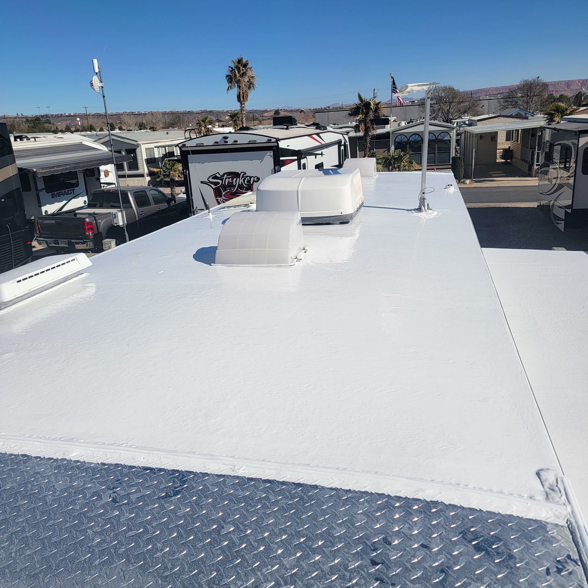 White RV roof with vents, diamond-plate front, and surrounding RV park under a blue sky.