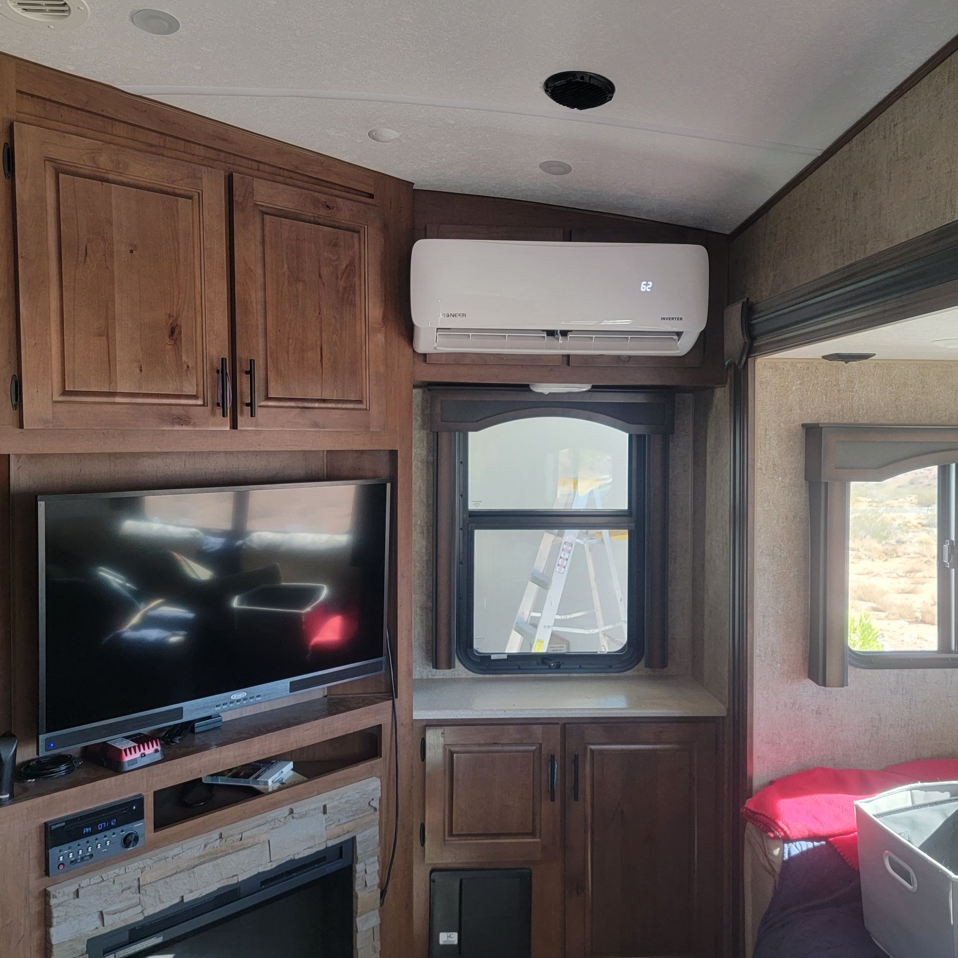RV interior with TV, cabinetry, air conditioner, and window.