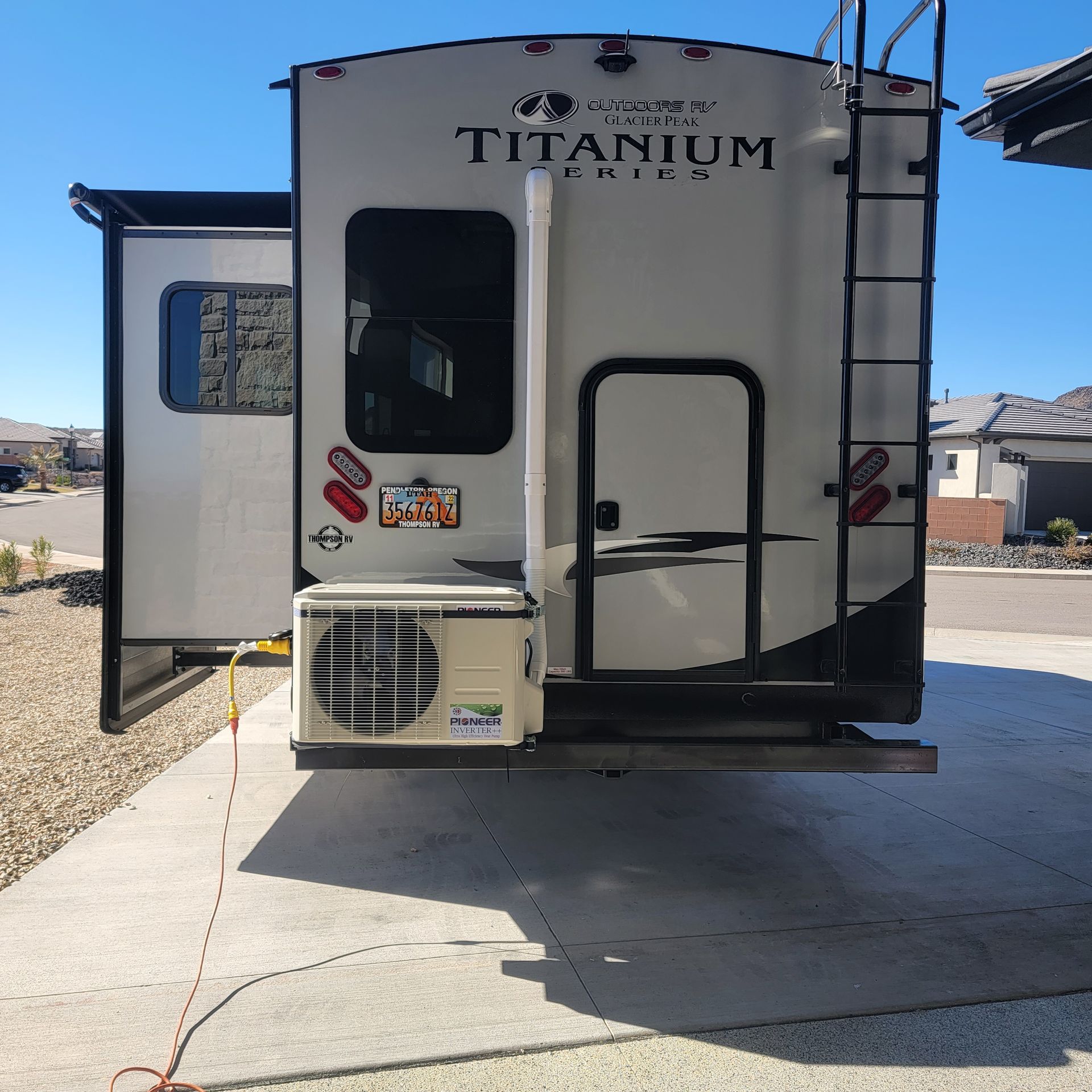 A travel trailer with an air conditioner attached, parked on a driveway.