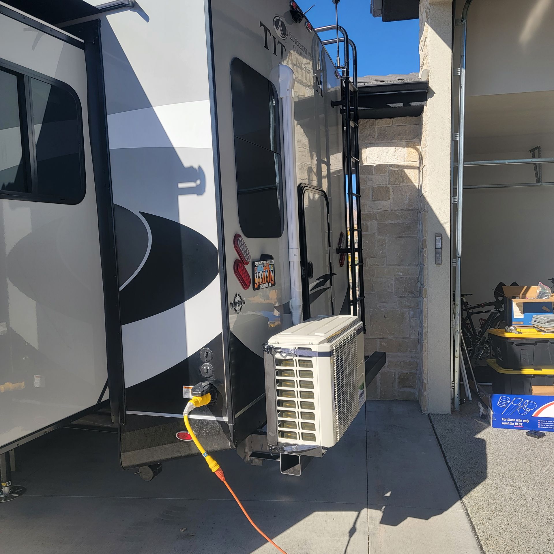 RV parked next to a wall, with an attached air conditioner and ladder.