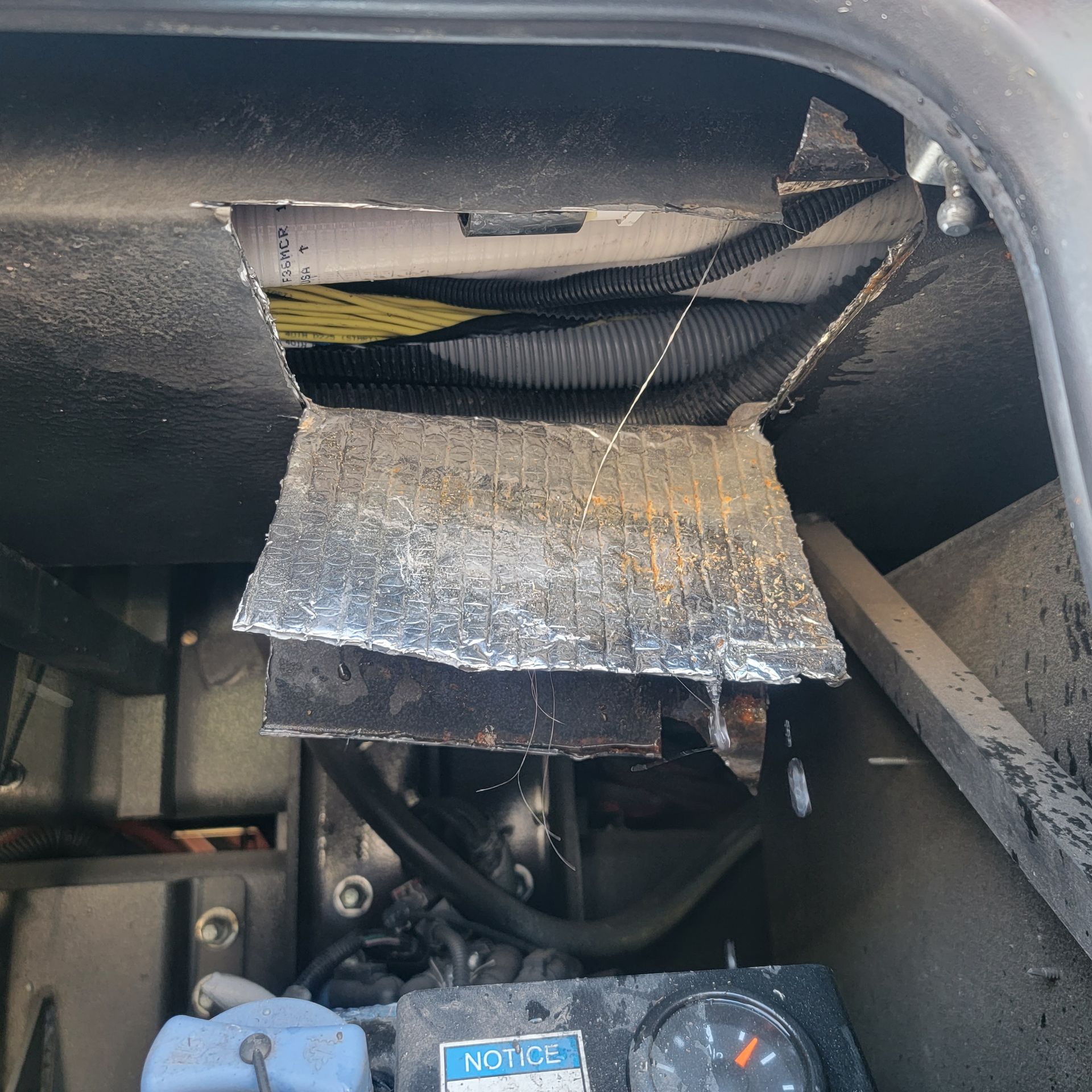 Hole in the roof of a vehicle compartment, revealing insulation and machinery.