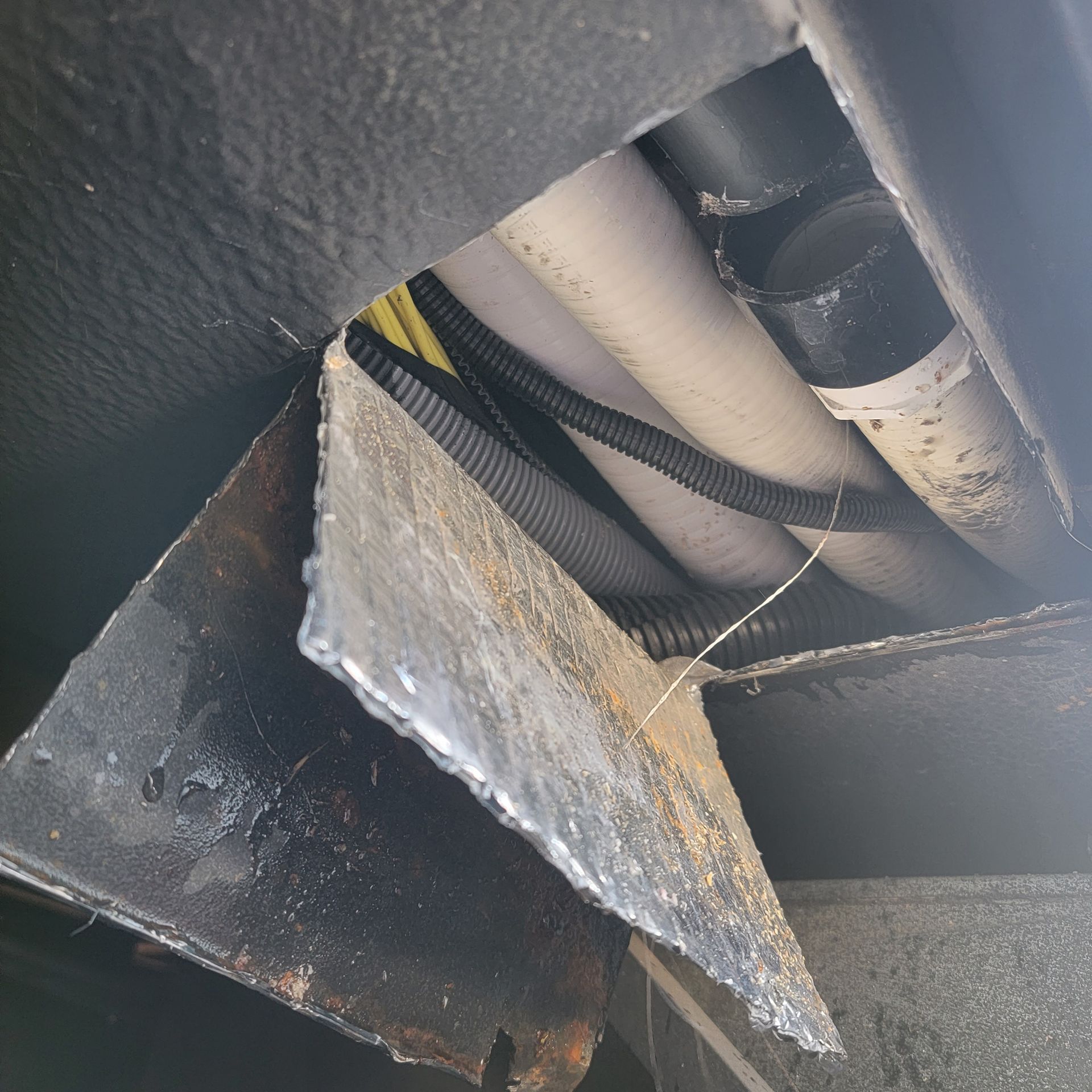 Underside view showing pipes, wiring, and a metal bracket of a vehicle, possibly an RV.