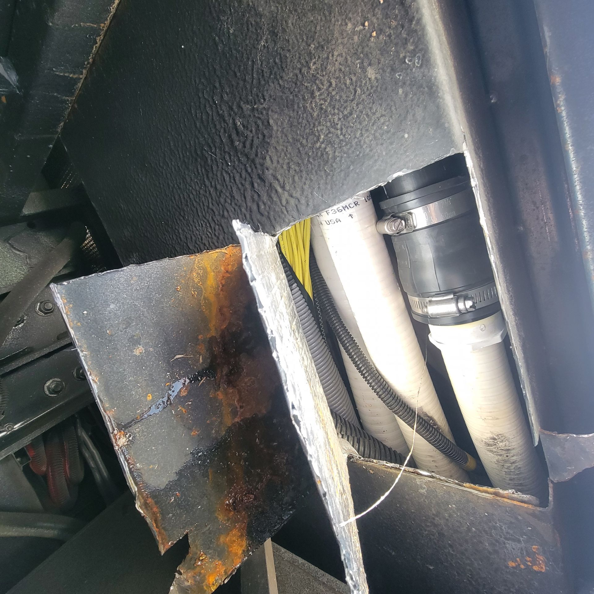 Inside a dark enclosure, a black hose connects to white pipes, secured by clamps.