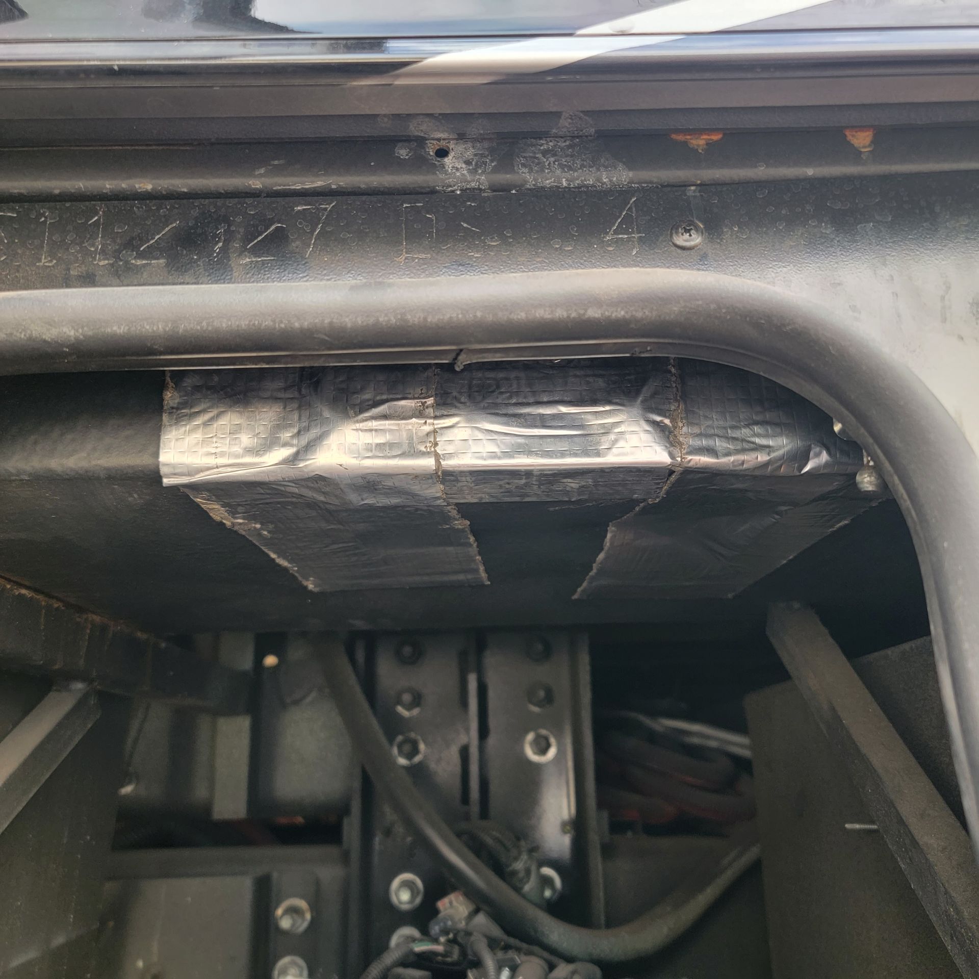 Black vehicle underside with duct tape securing something.