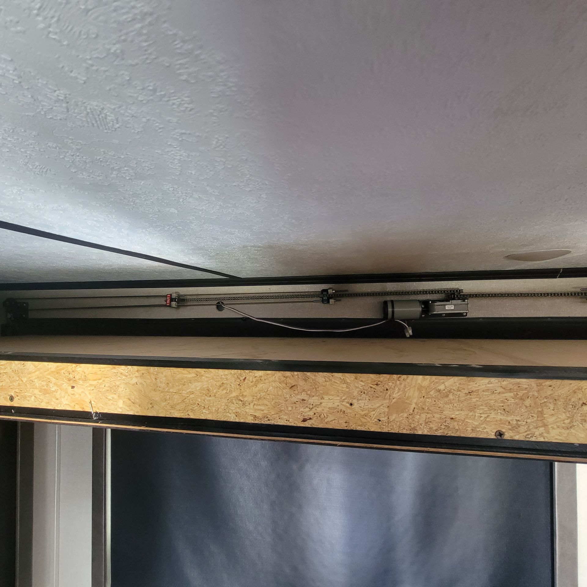 View of a ceiling with a wooden beam and a chain-driven mechanism, possibly for a door or shutter.