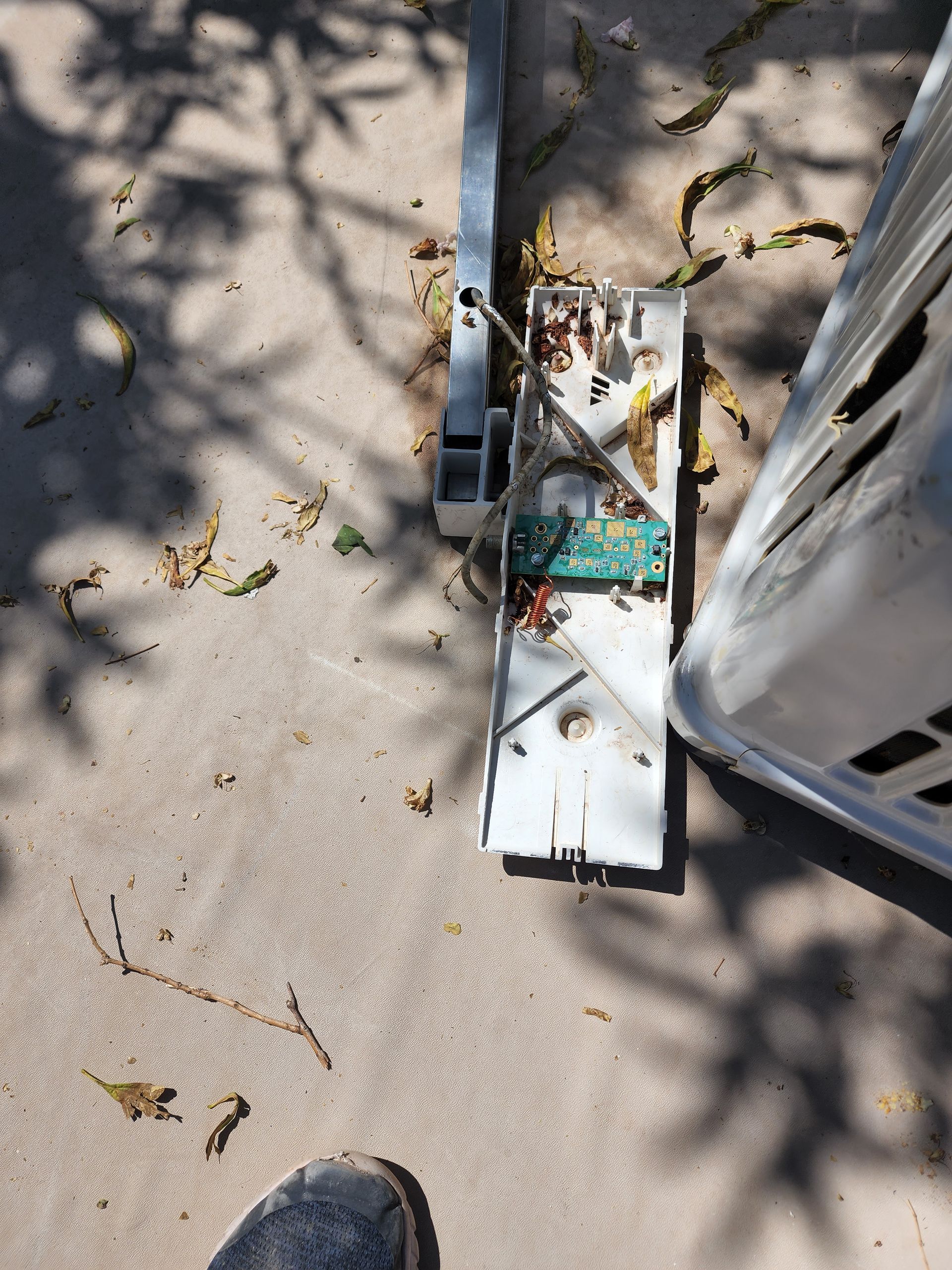 Broken metal and electronic components on a concrete surface, with a shoe and shadow visible.