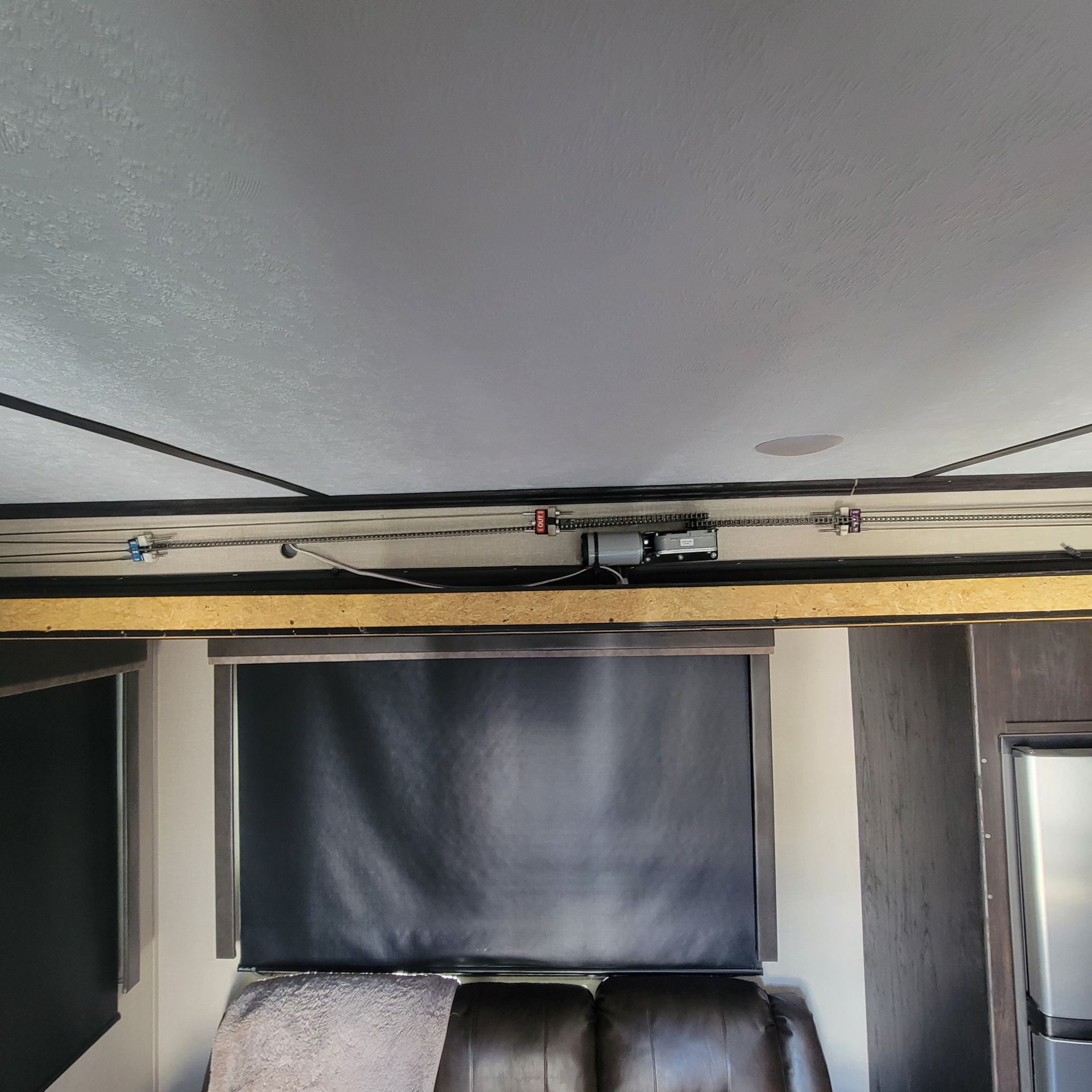 RV interior ceiling with window, couch, and cabinets. Black window shade.