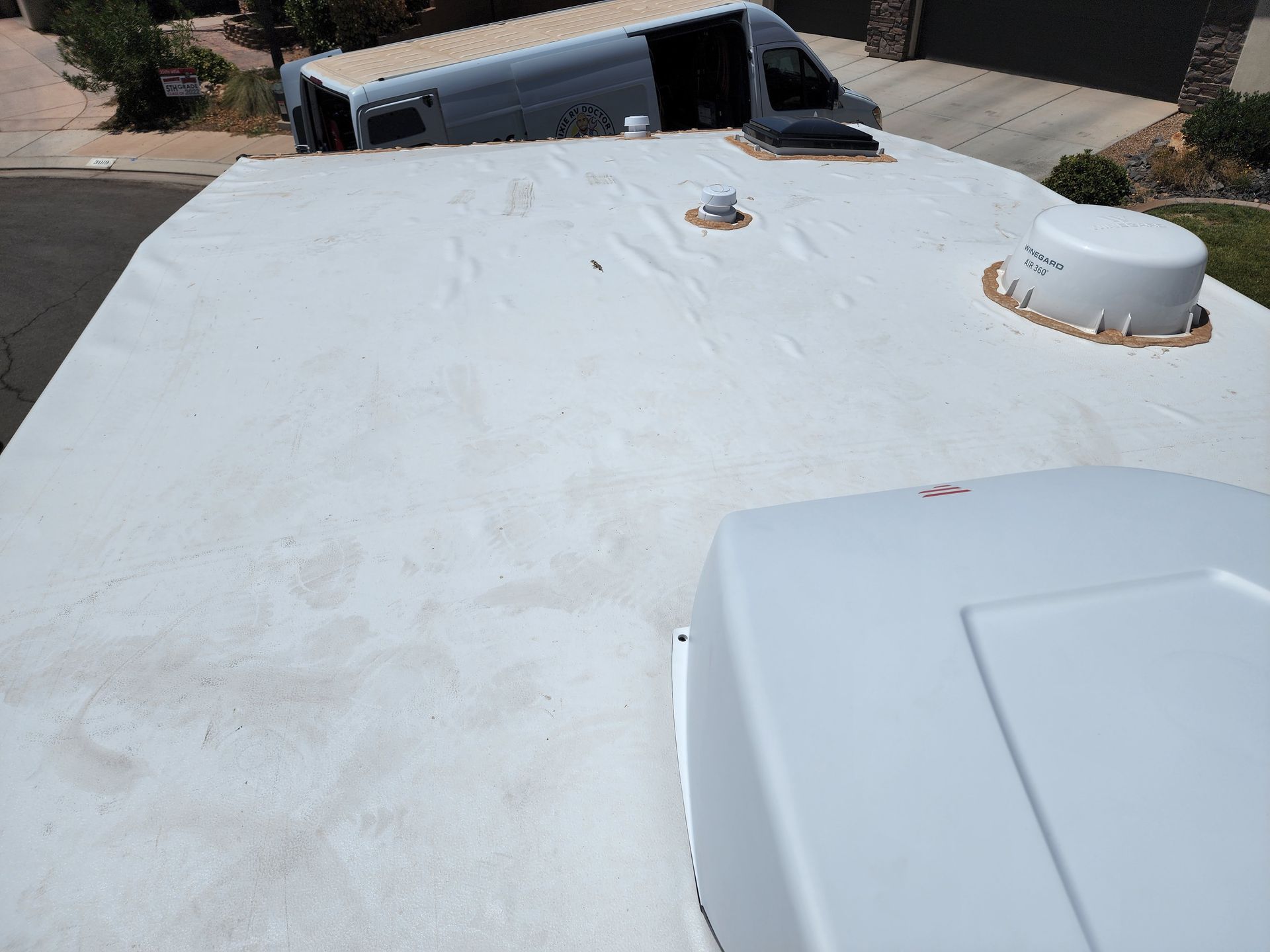 White RV roof with stains, air conditioning unit, vents, and satellite dome.