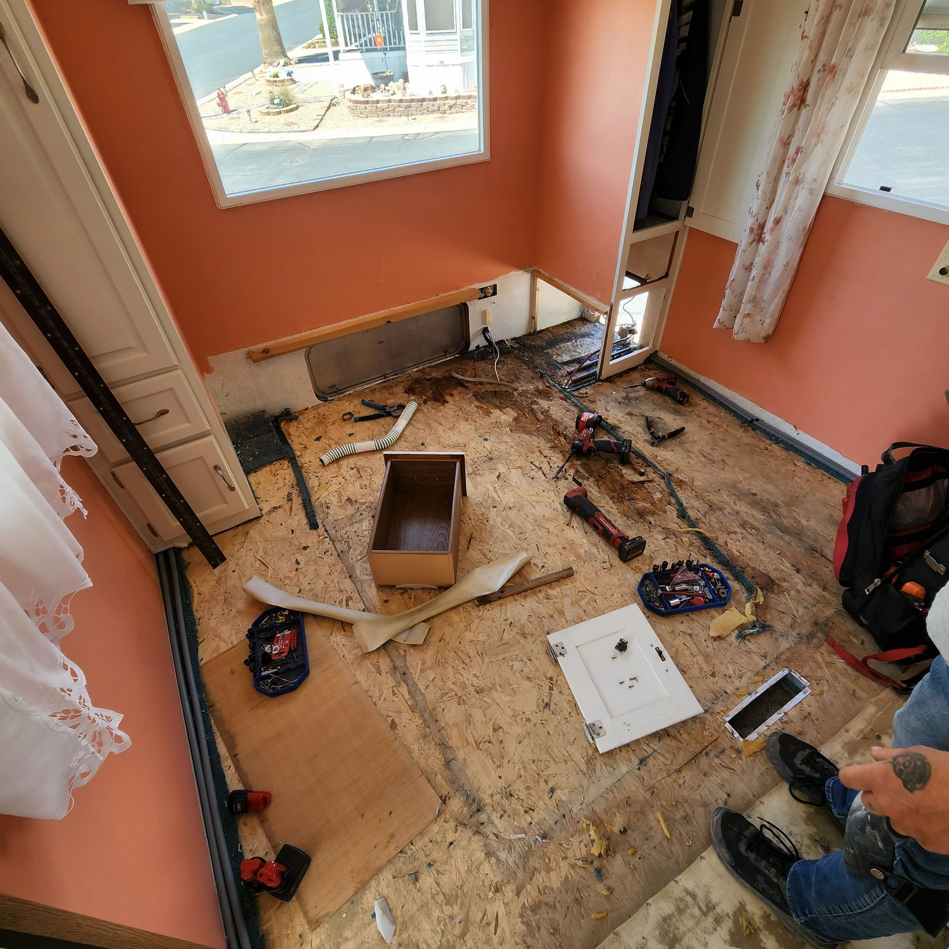 Room under construction with exposed subfloor, tools, and a partial view of a person's legs.