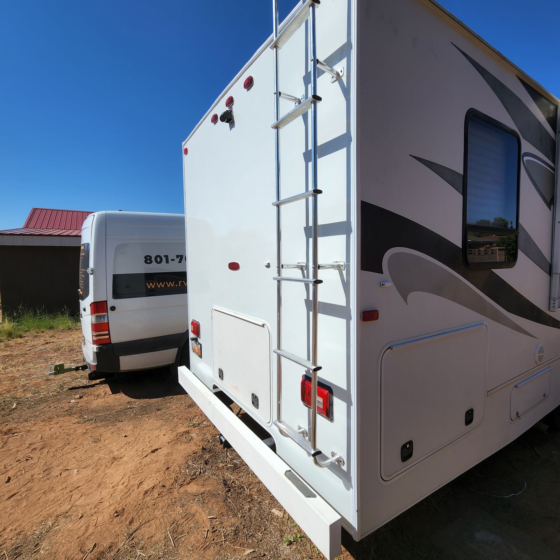 White RV with a ladder parked next to a white van on a sunny day.