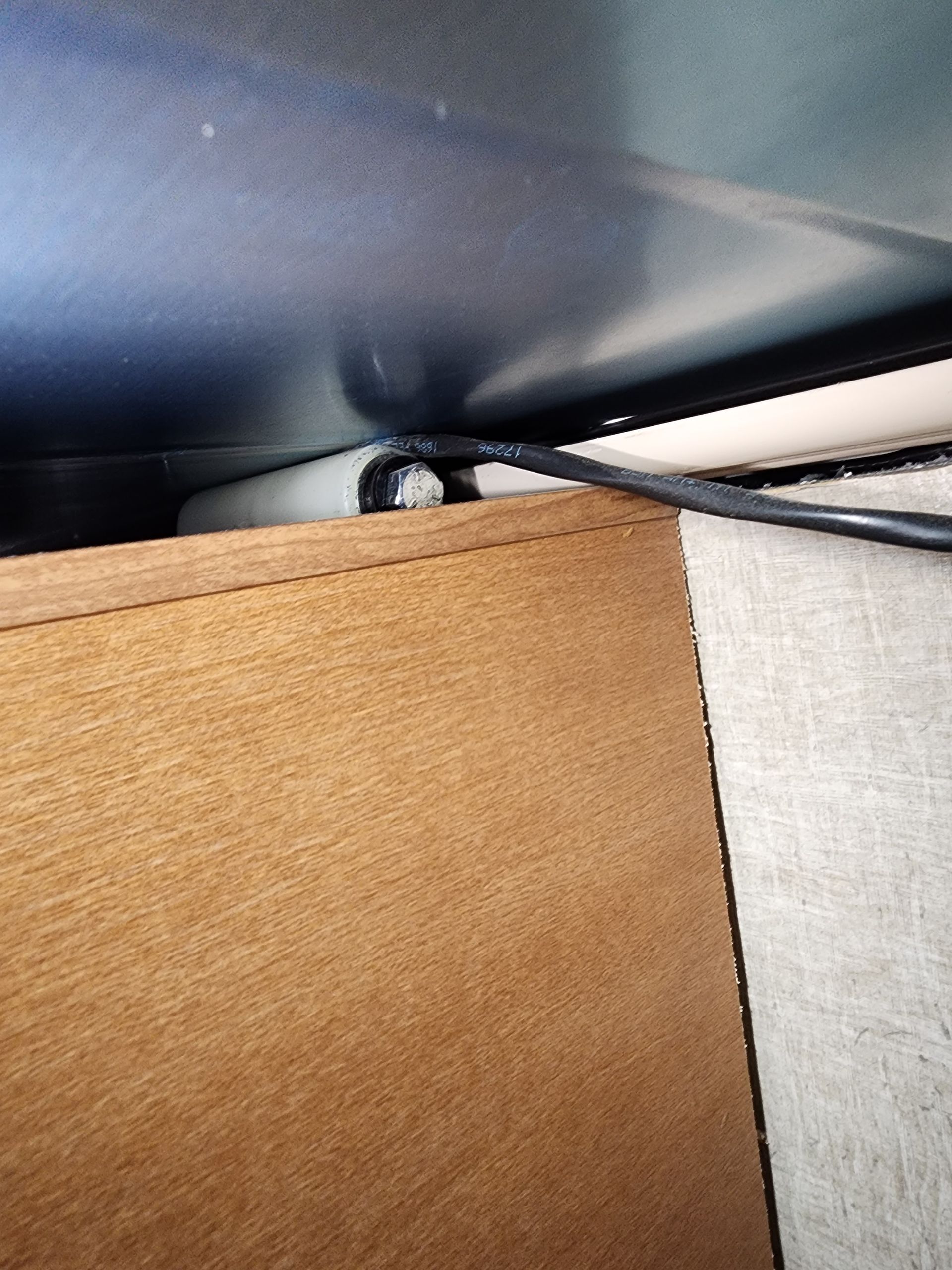 Tan fabric edge beneath a dark metallic surface. A white plastic tube and black cable are visible.