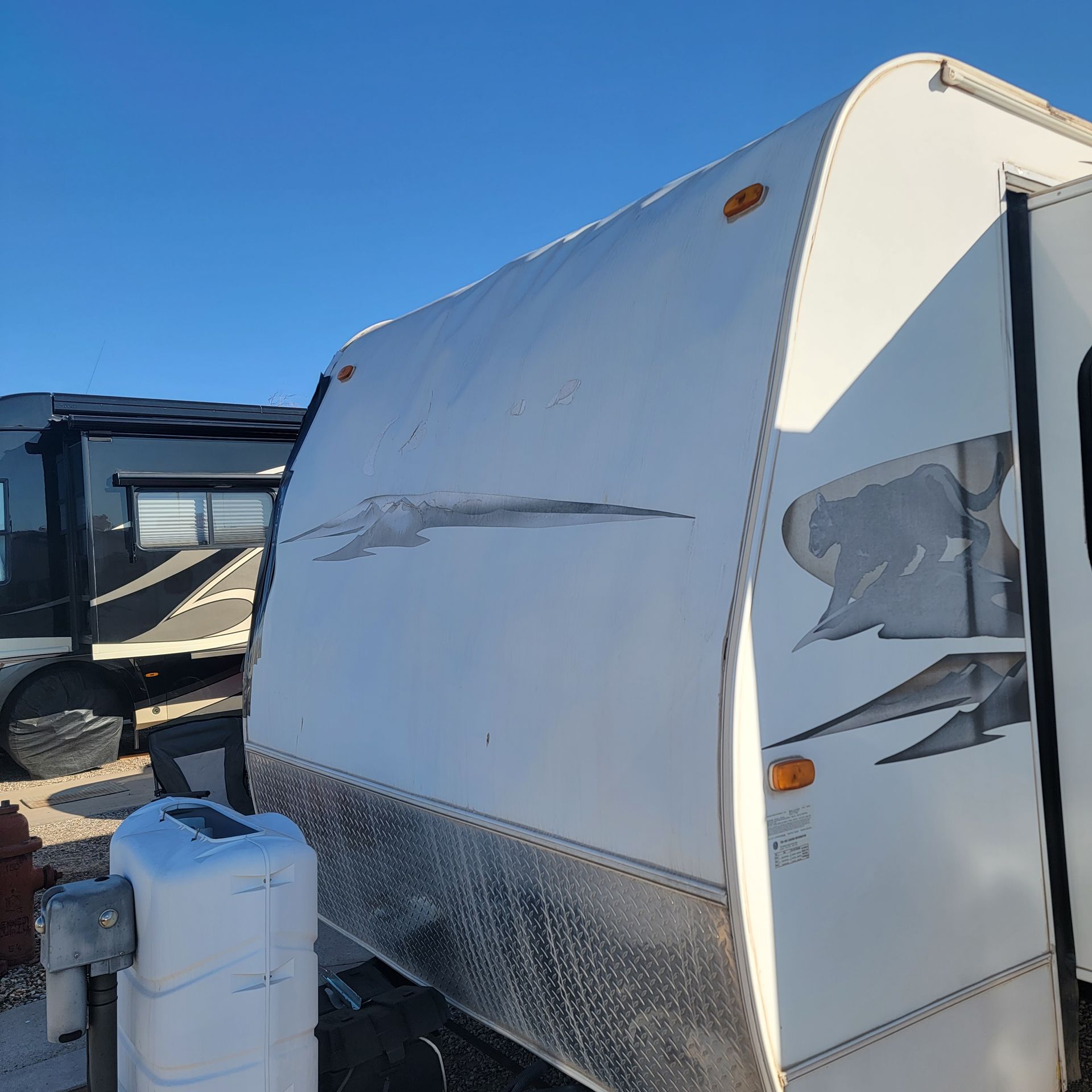 White travel trailer with gray graphics parked outside on a sunny day.