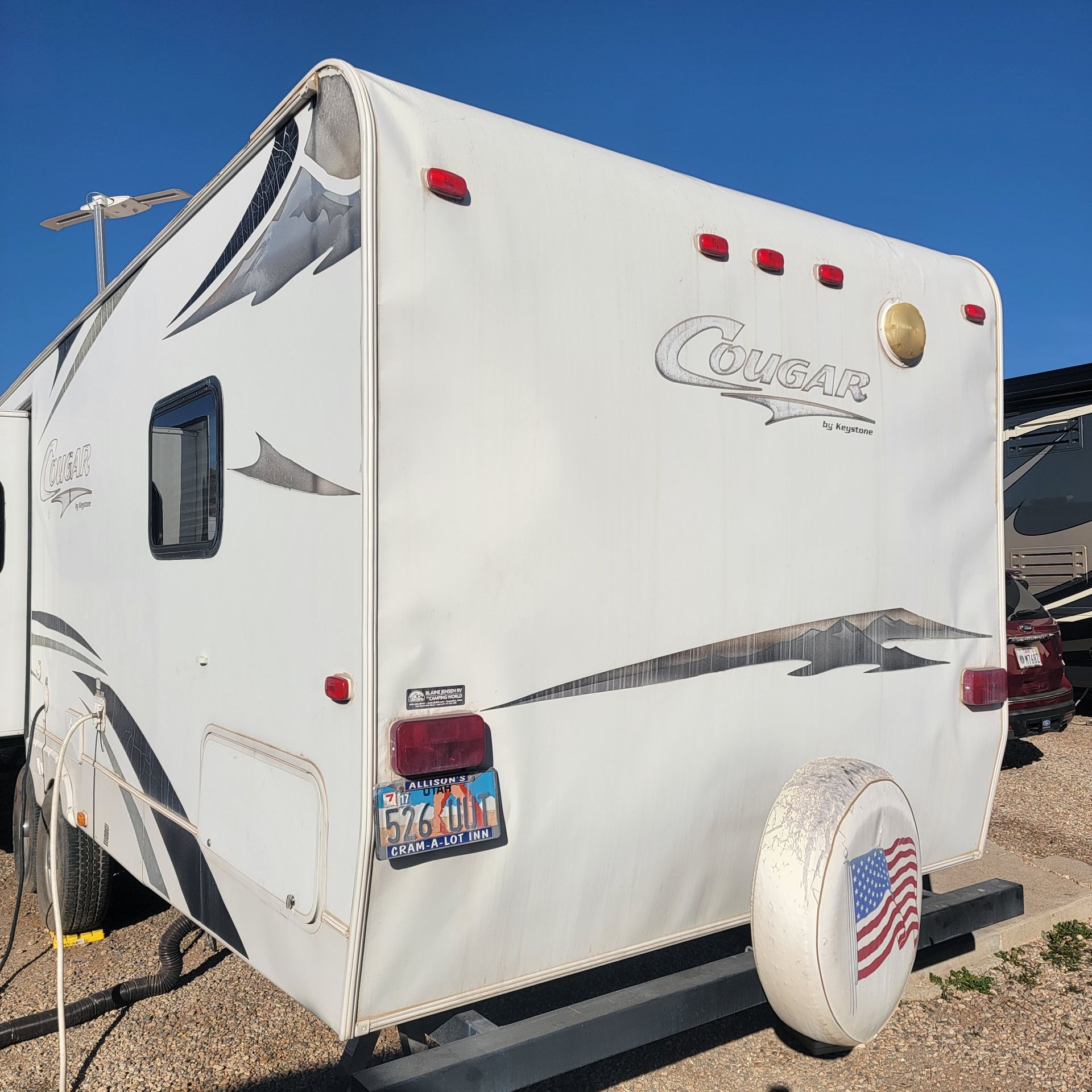 White Cougar travel trailer with Utah license plate, spare tire cover featuring American flag.