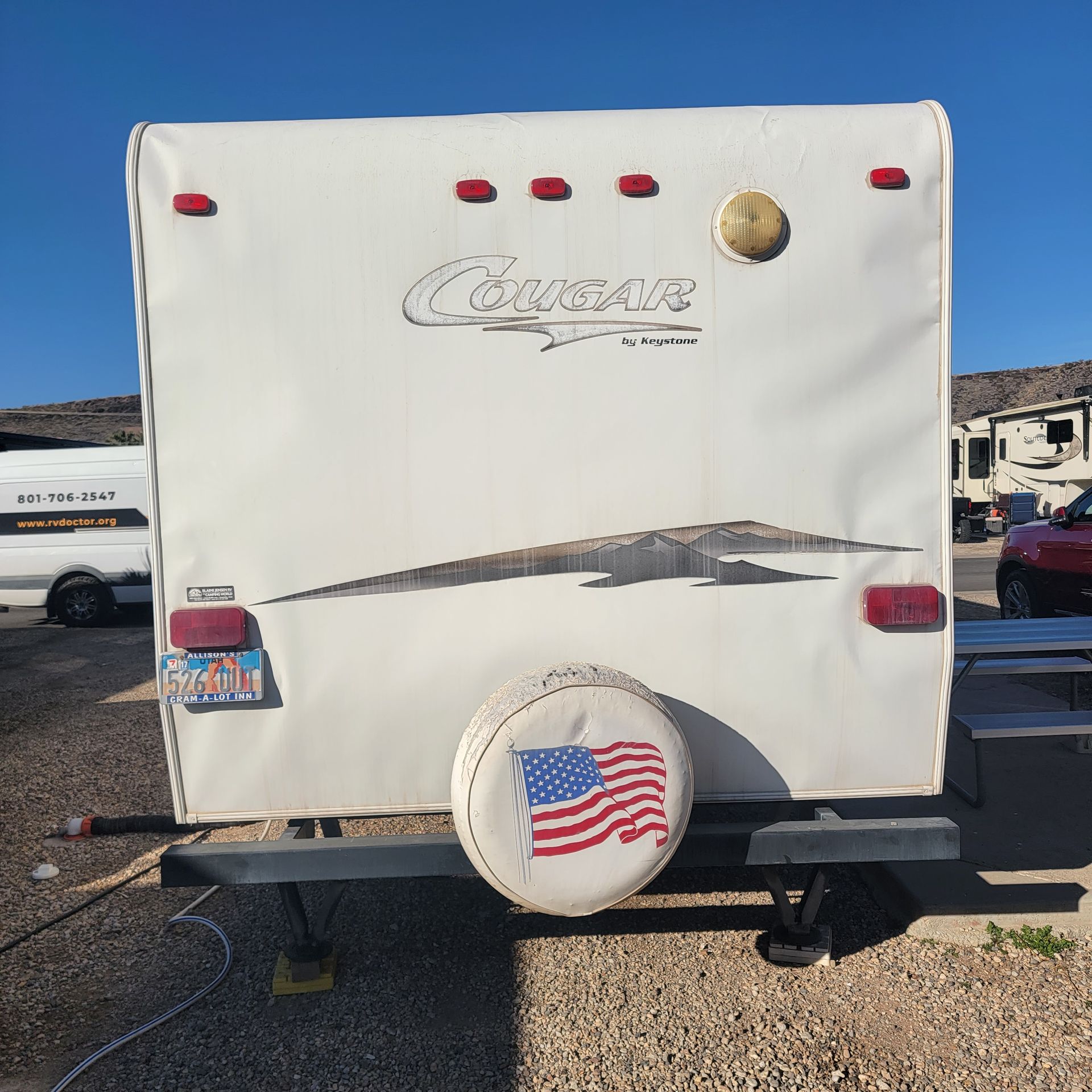 Rear view of a white Cougar travel trailer with a spare tire cover showing an American flag.