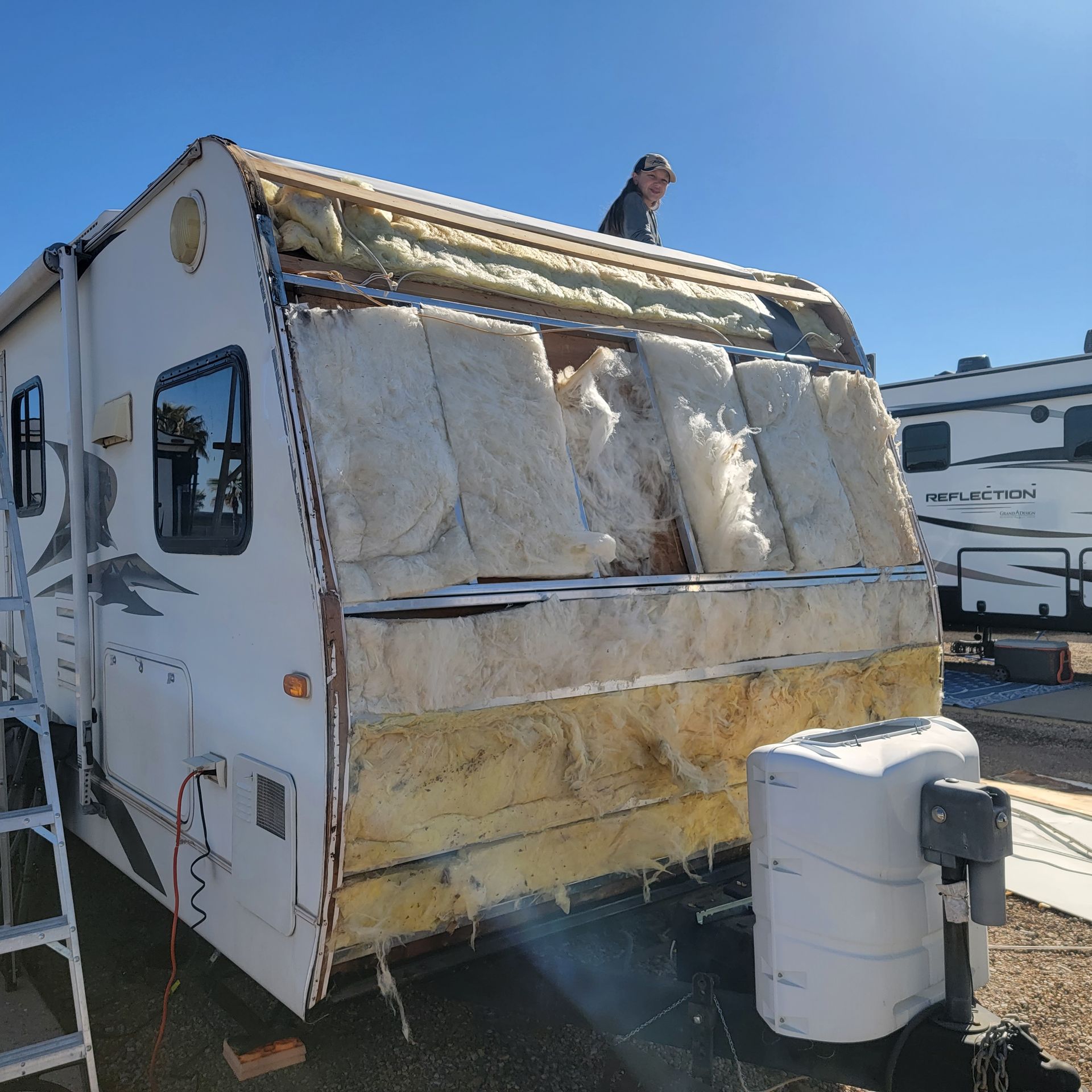 RV with front exterior dismantled, exposing insulation, person on roof.