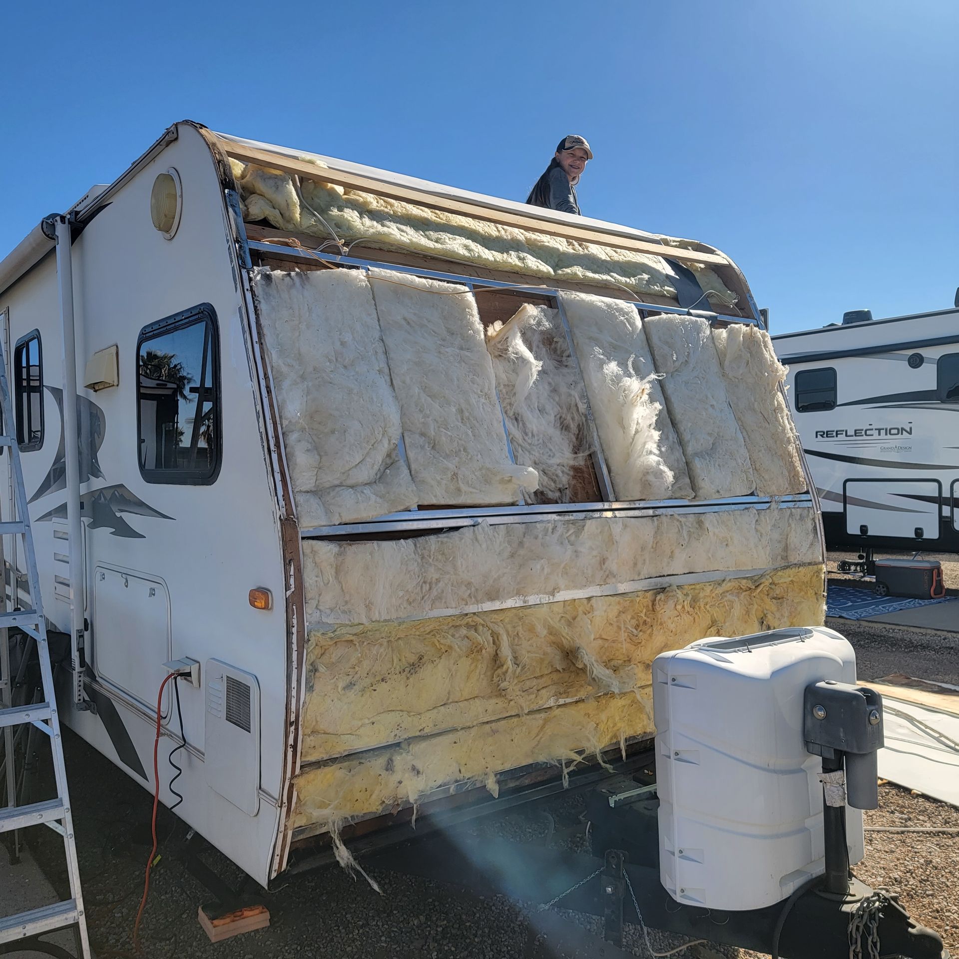 RV with exposed insulation, being worked on by a person on the roof.