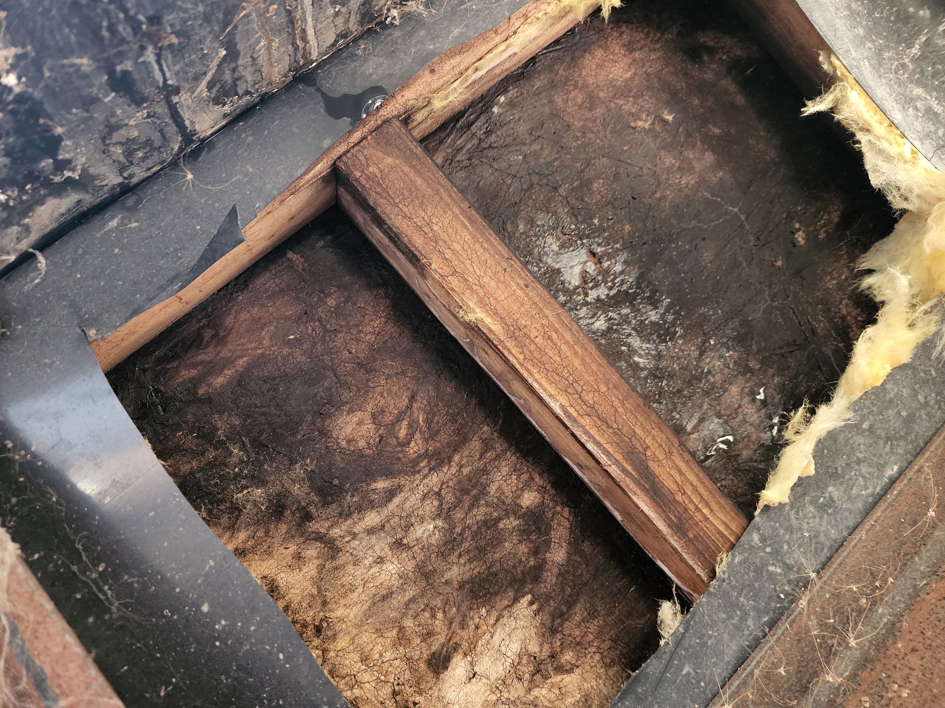 Wooden beams and dark, stained surface inside a structure, possibly damaged.