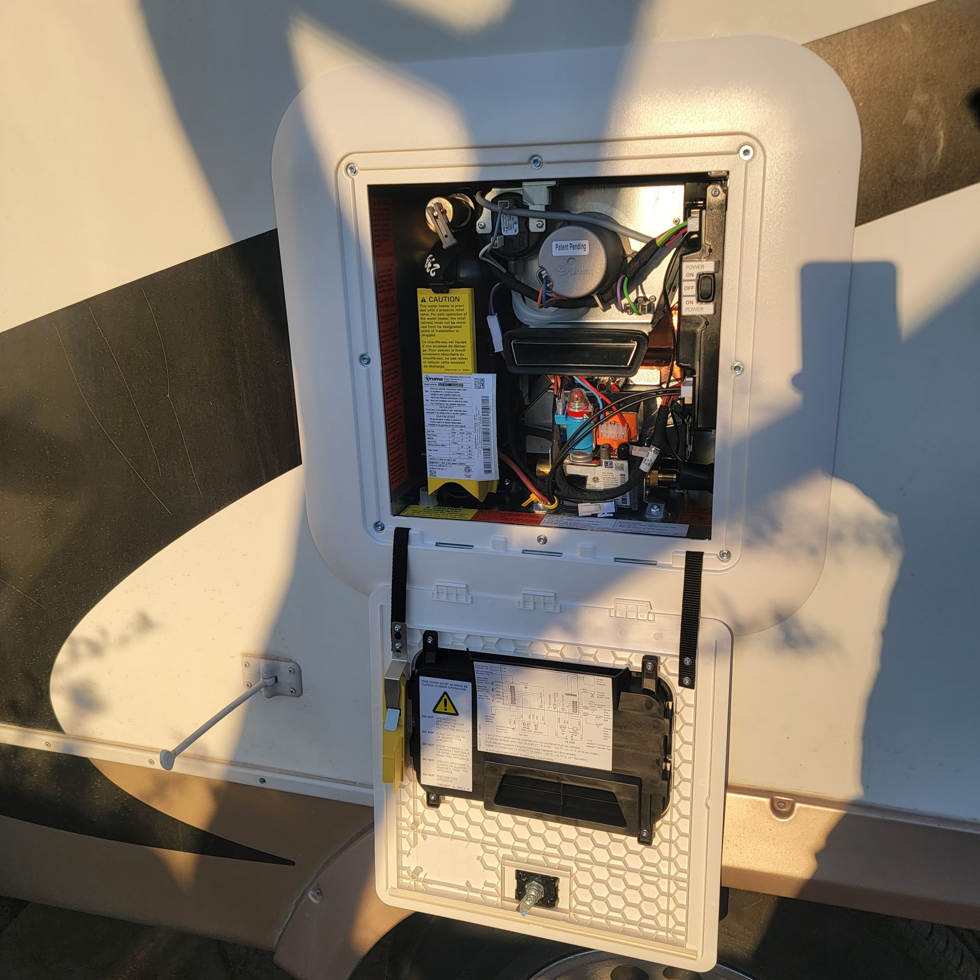 RV water heater access panel open, revealing internal components. White, beige, and black colors.
