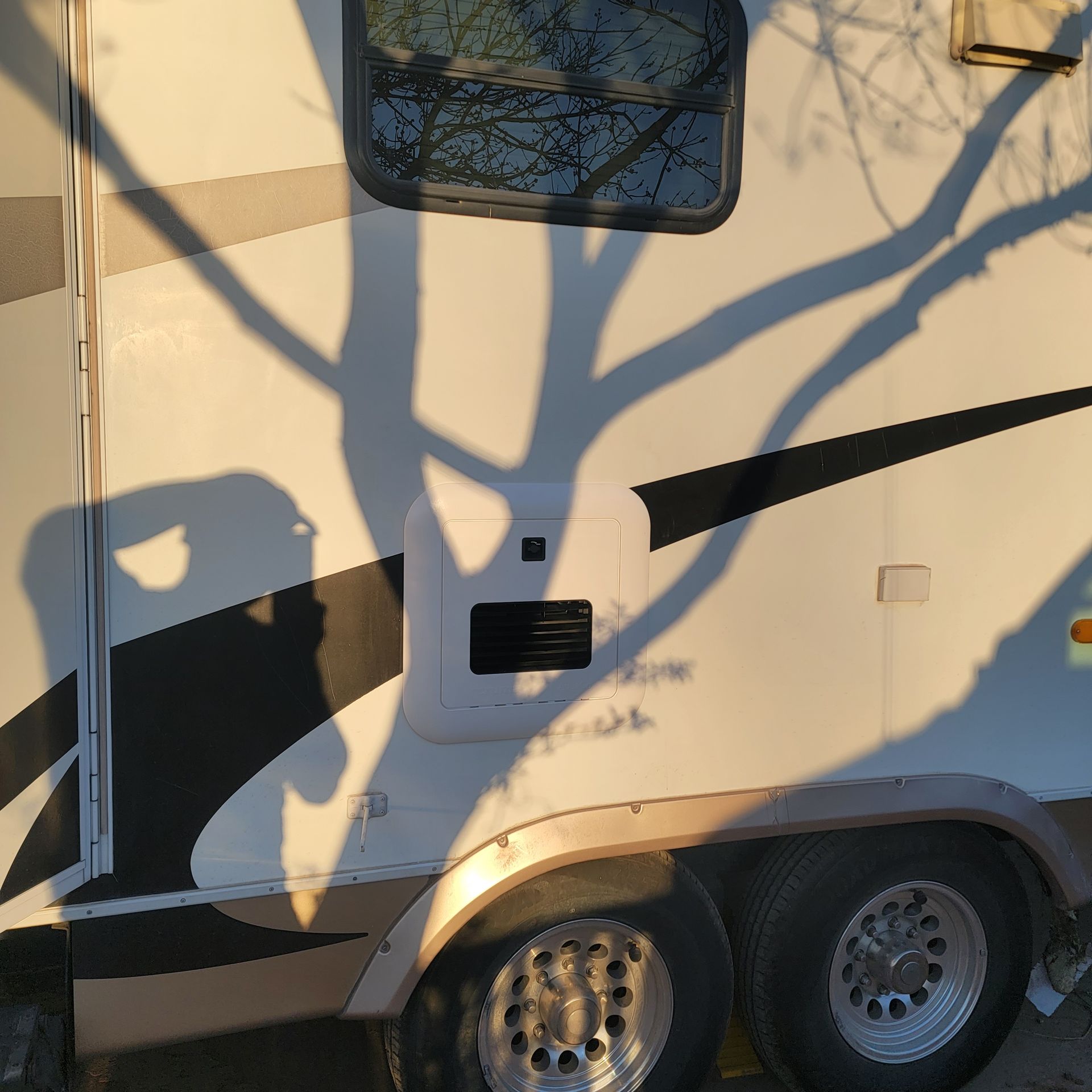 White camper with black and tan accents, shadow of a tree cast on the side.
