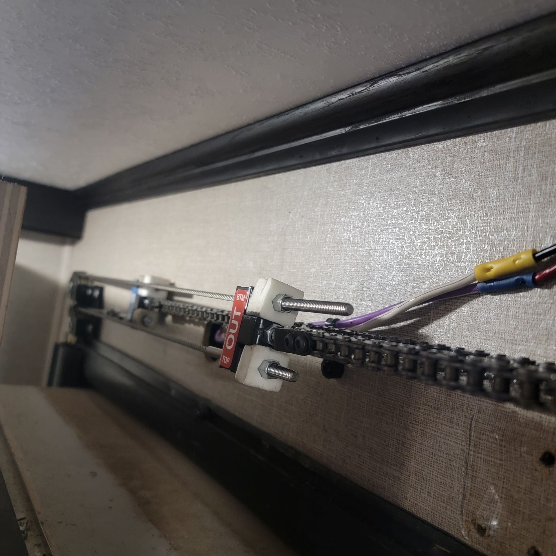 Motorized chain mechanism inside an RV slide-out, with wires and white plastic components.