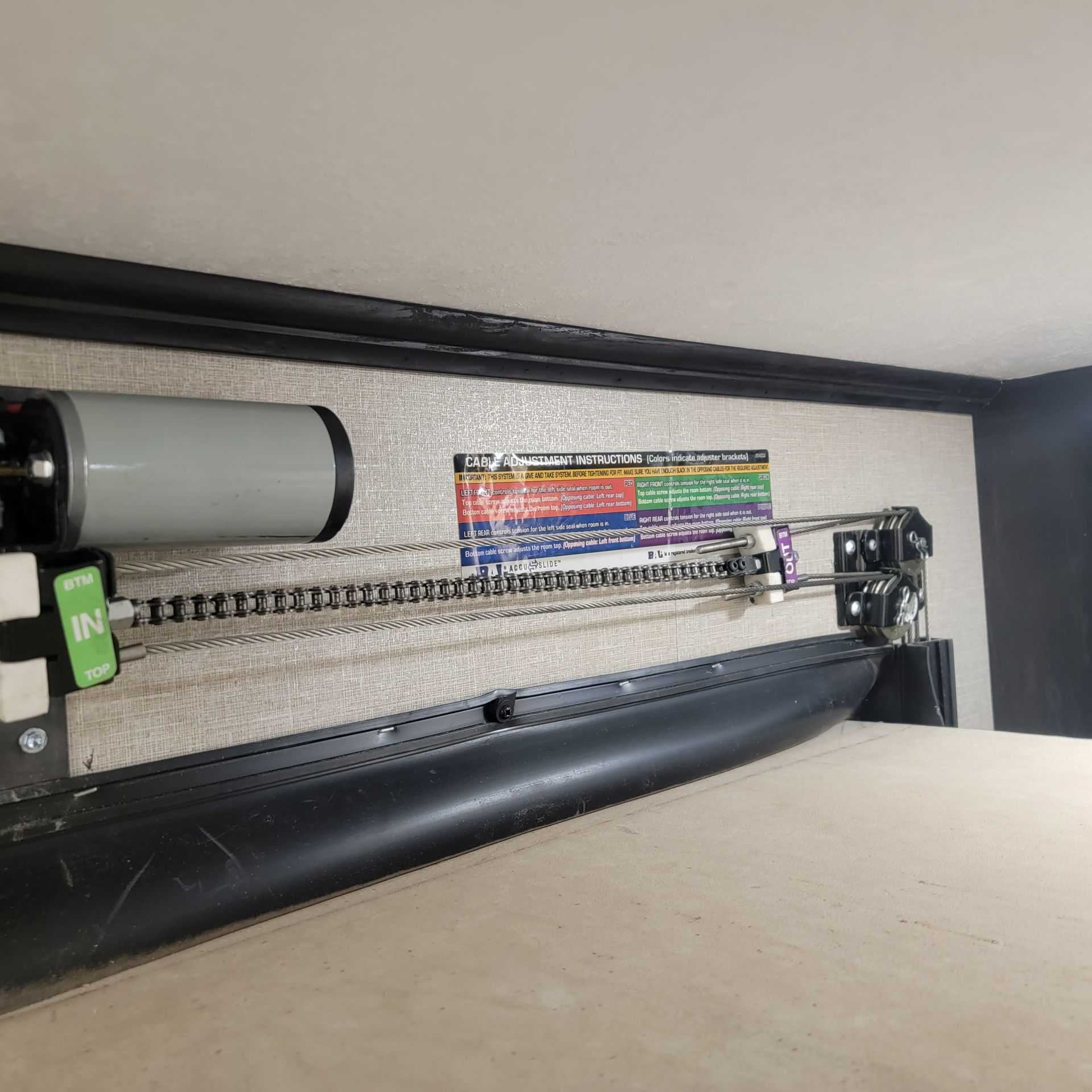 Close-up of a large black machine with a gray cylinder, a chain, and a printed sign against a wall.