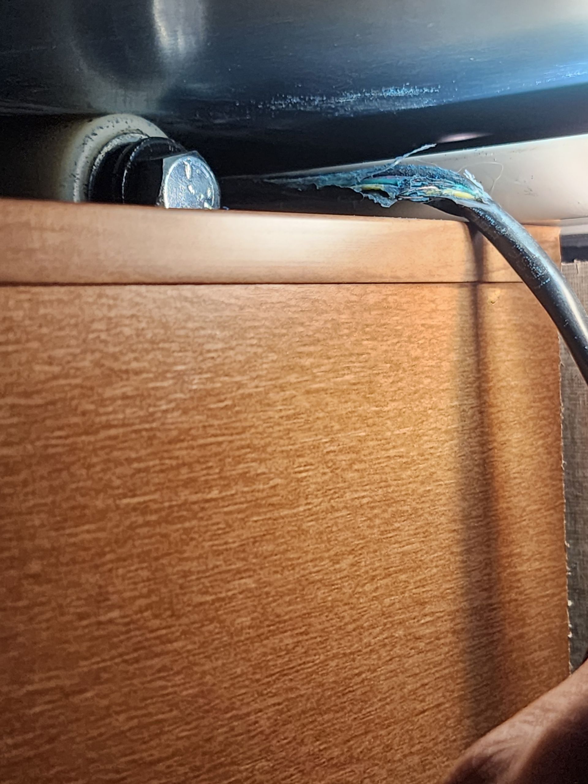 Underside of a sink: exposed wiring with damaged blue insulation. Brown cabinet below the sink.