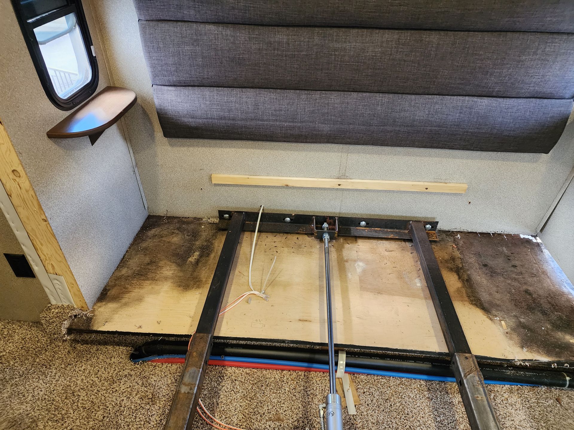 RV bed frame with damaged wood, mechanical lift, and plumbing visible.