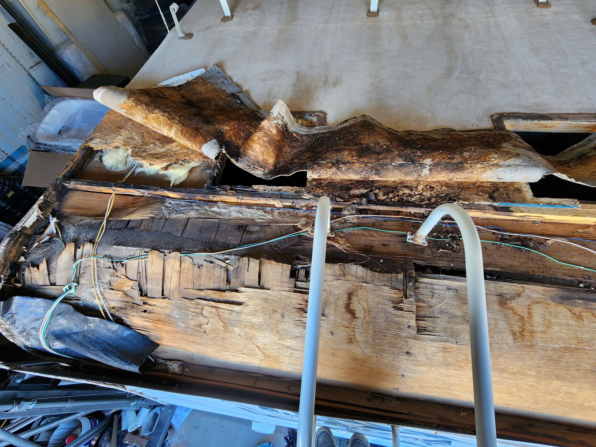 Severely damaged vehicle roof with decaying wood, exposed metal, and crumbling material.