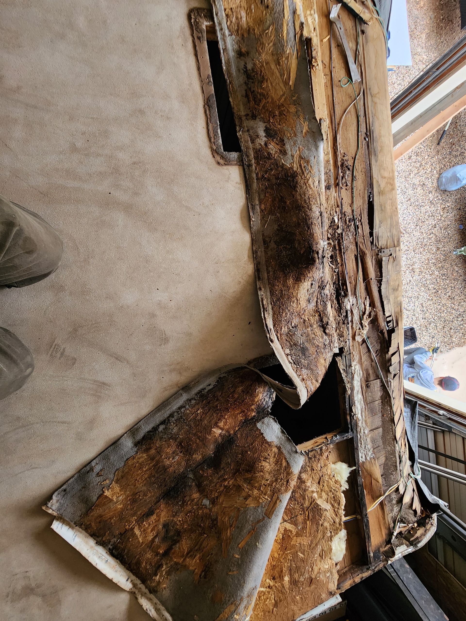 Damaged roof section with rotted wood and torn materials on a concrete floor.