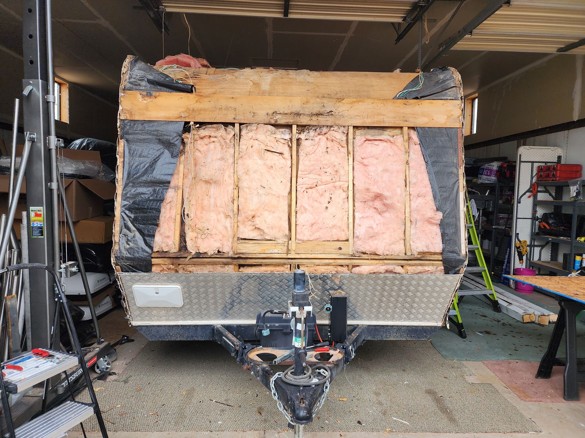 RV front with exposed insulation, wood framing, and aluminum diamond plating, in a garage.