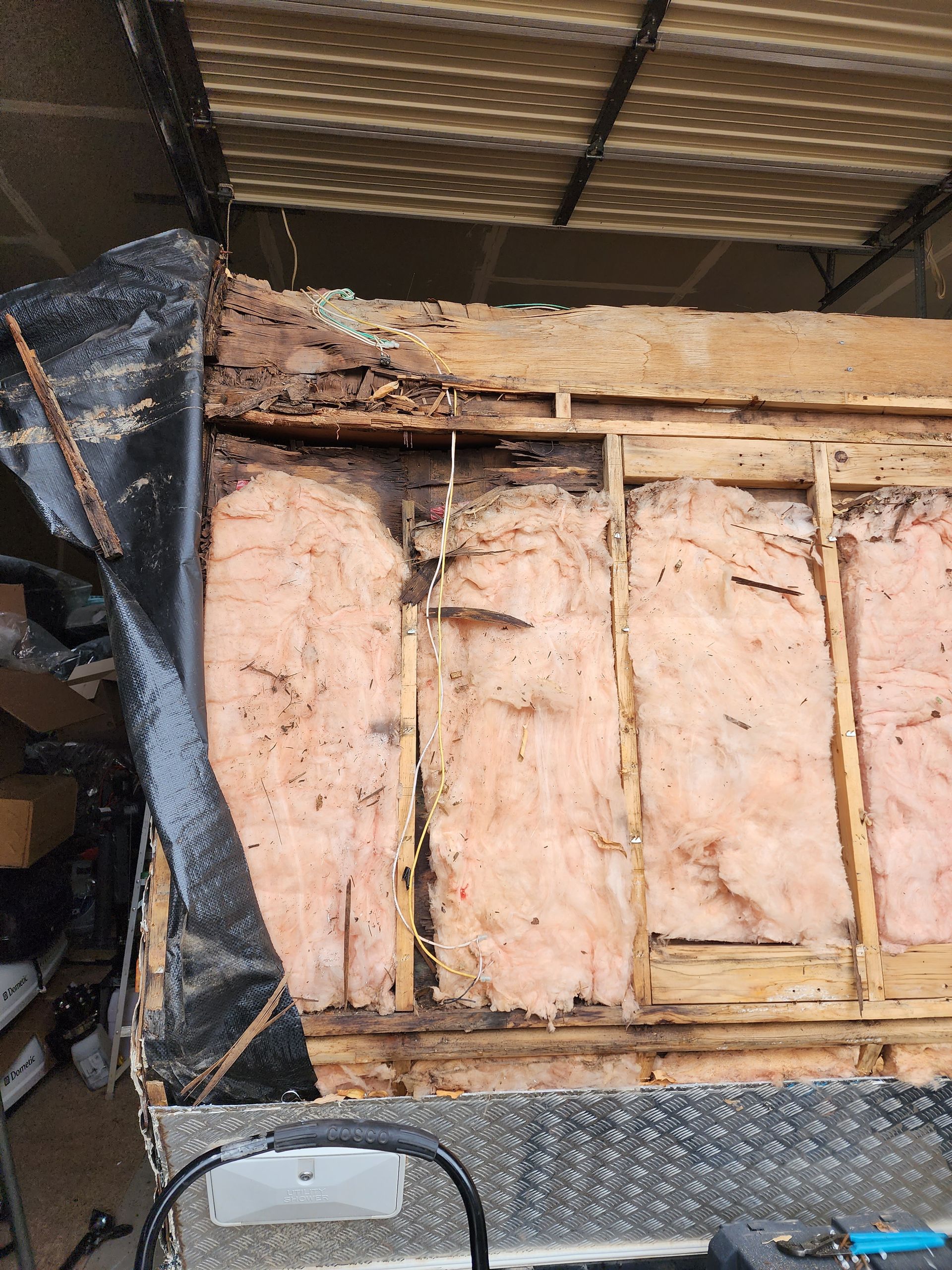 Exterior wall damage exposing insulation and wooden framing under a tarp.