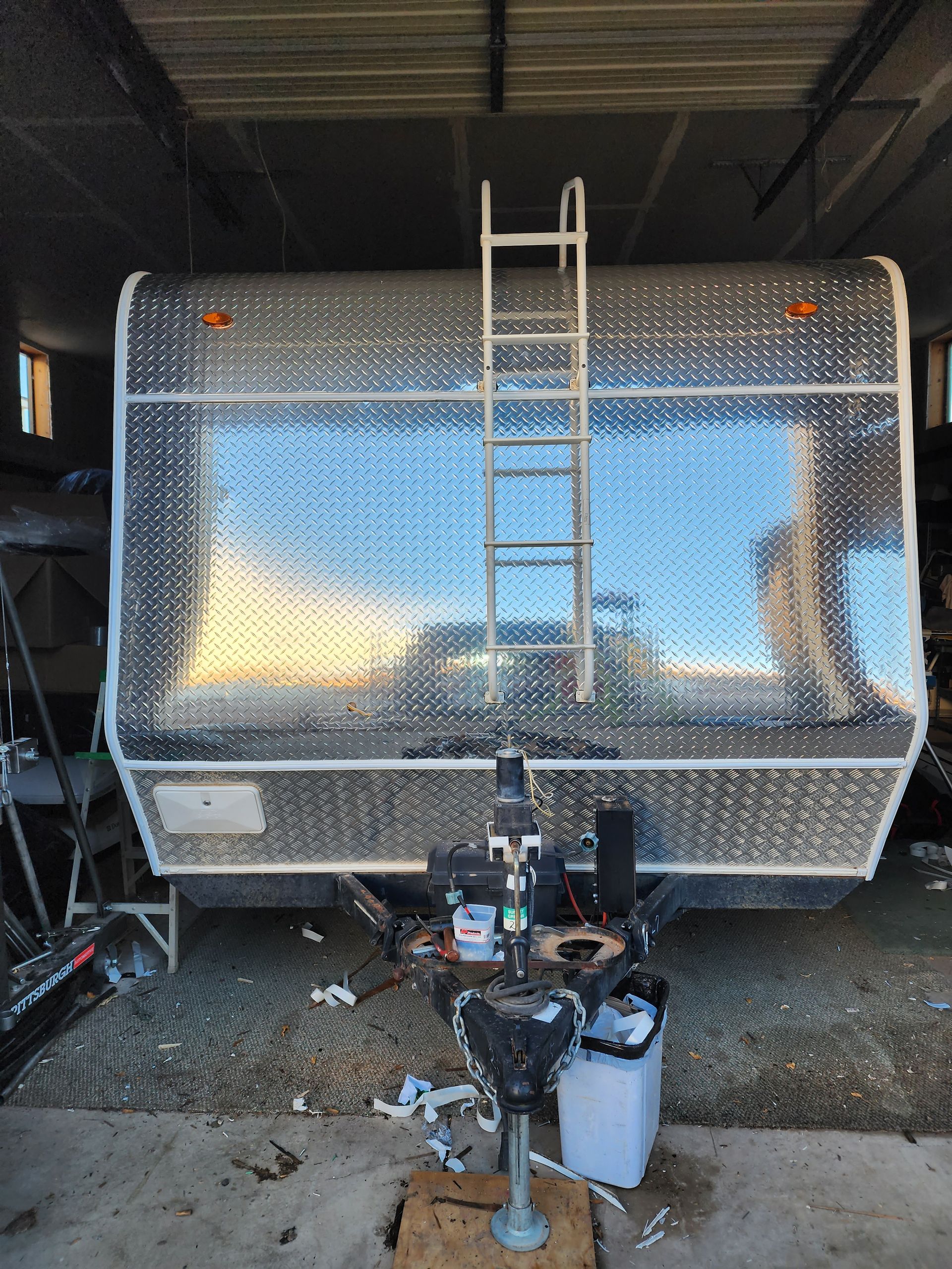 Silver camper trailer with ladder, in a garage.
