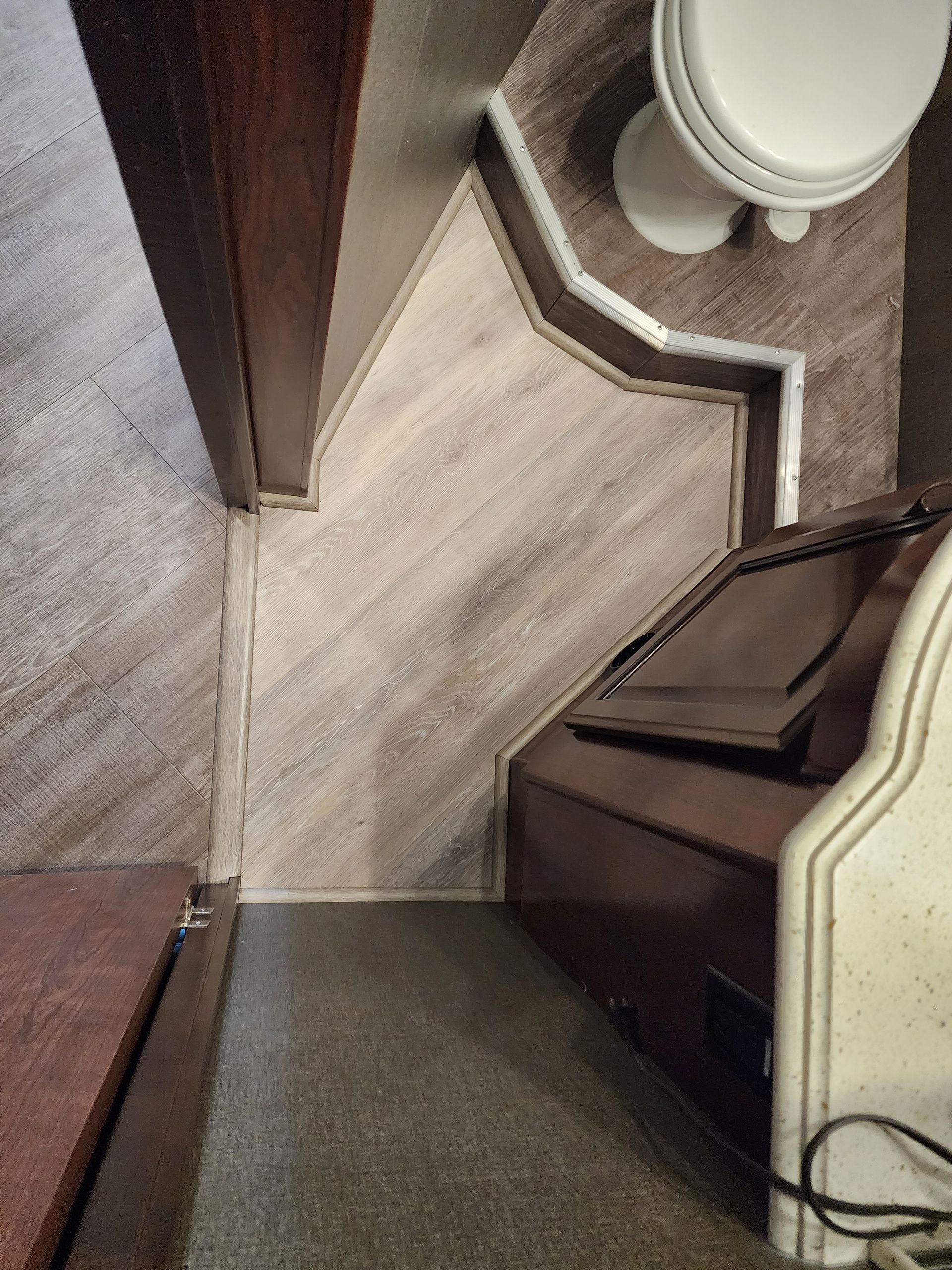 Bathroom corner with light-colored flooring, toilet, and dark brown cabinetry. Beige and brown tones throughout.