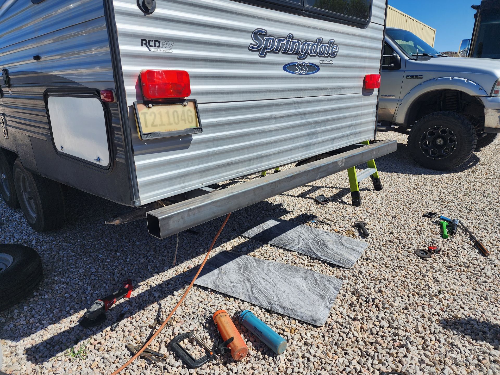 RV back end with bumper, license plate, and ramps on gravel.