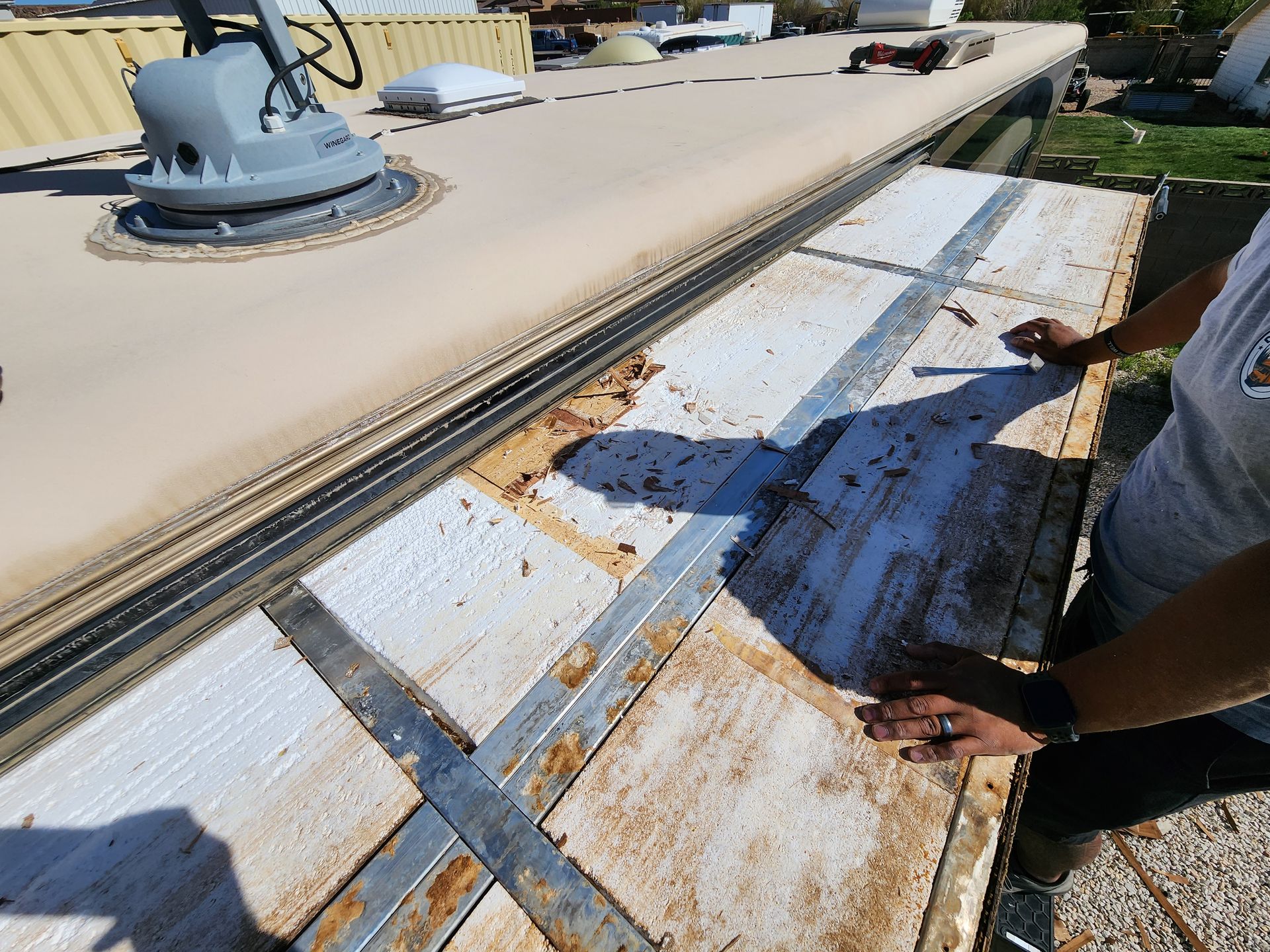 Person inspecting RV roof with exposed insulation and metal support beams.