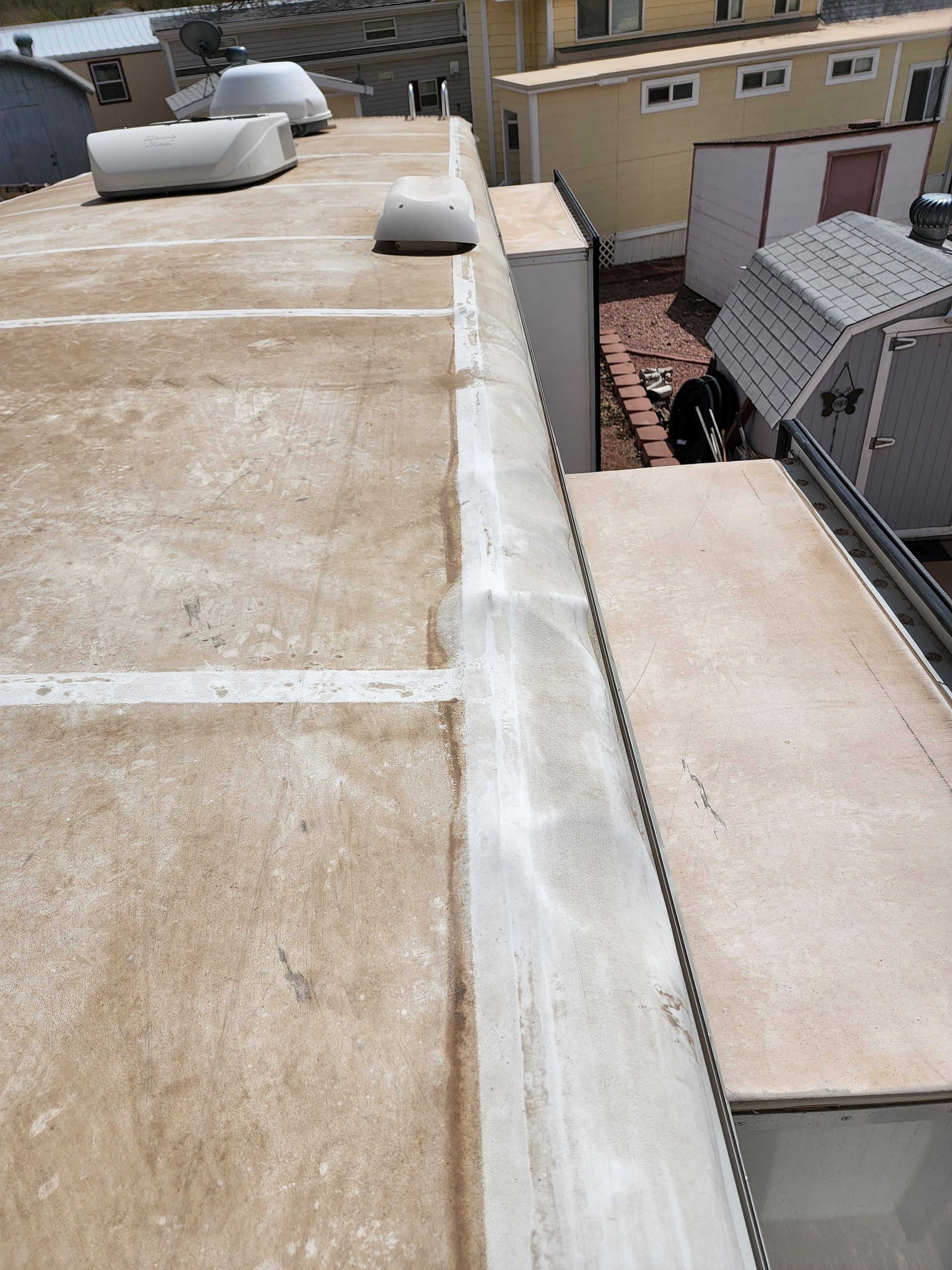 RV roof with discoloration and caulking along the edges, with buildings in the background.