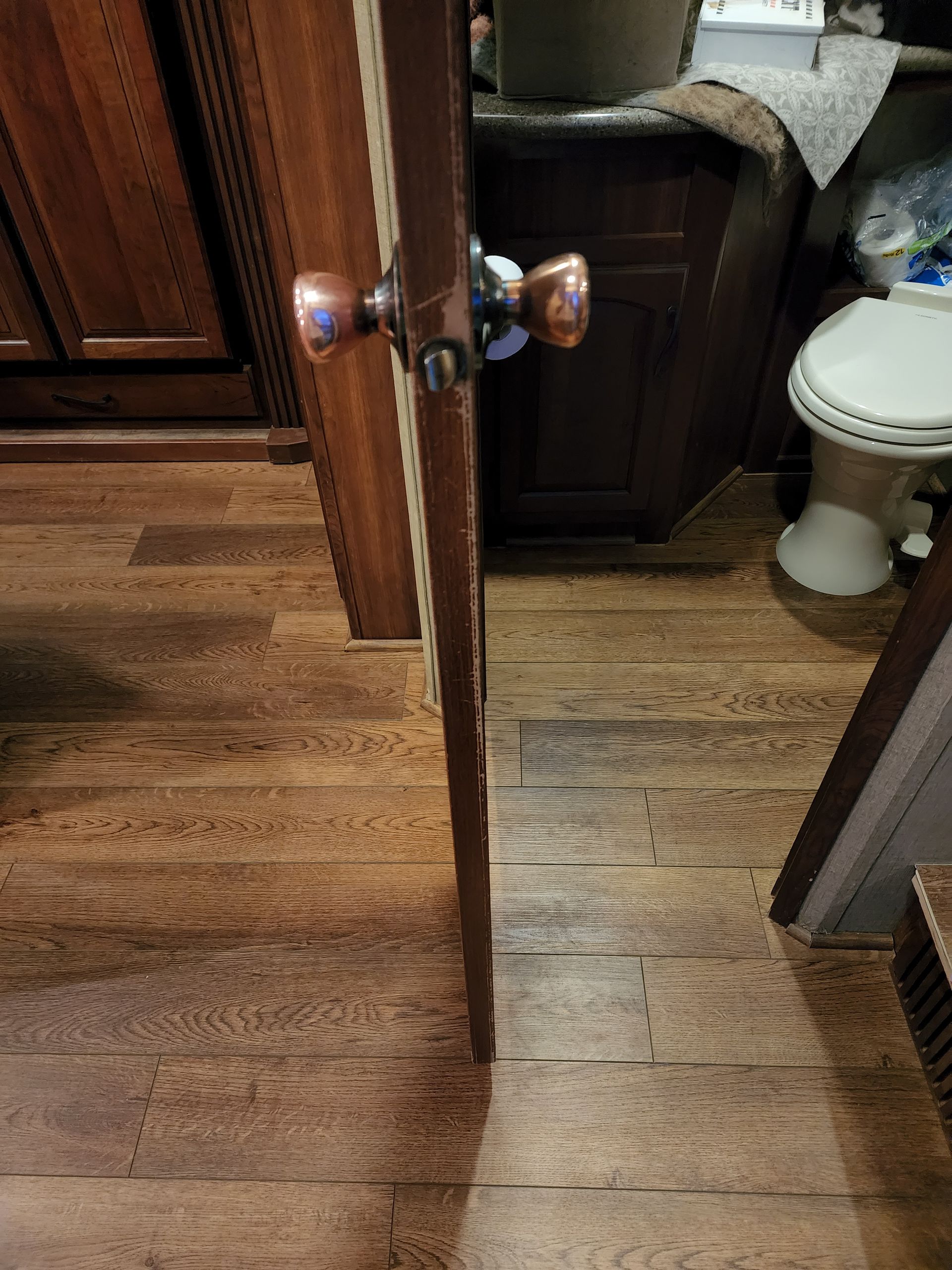 Brown door with copper doorknob slightly ajar, wood floor, dark cabinetry, and a toilet.