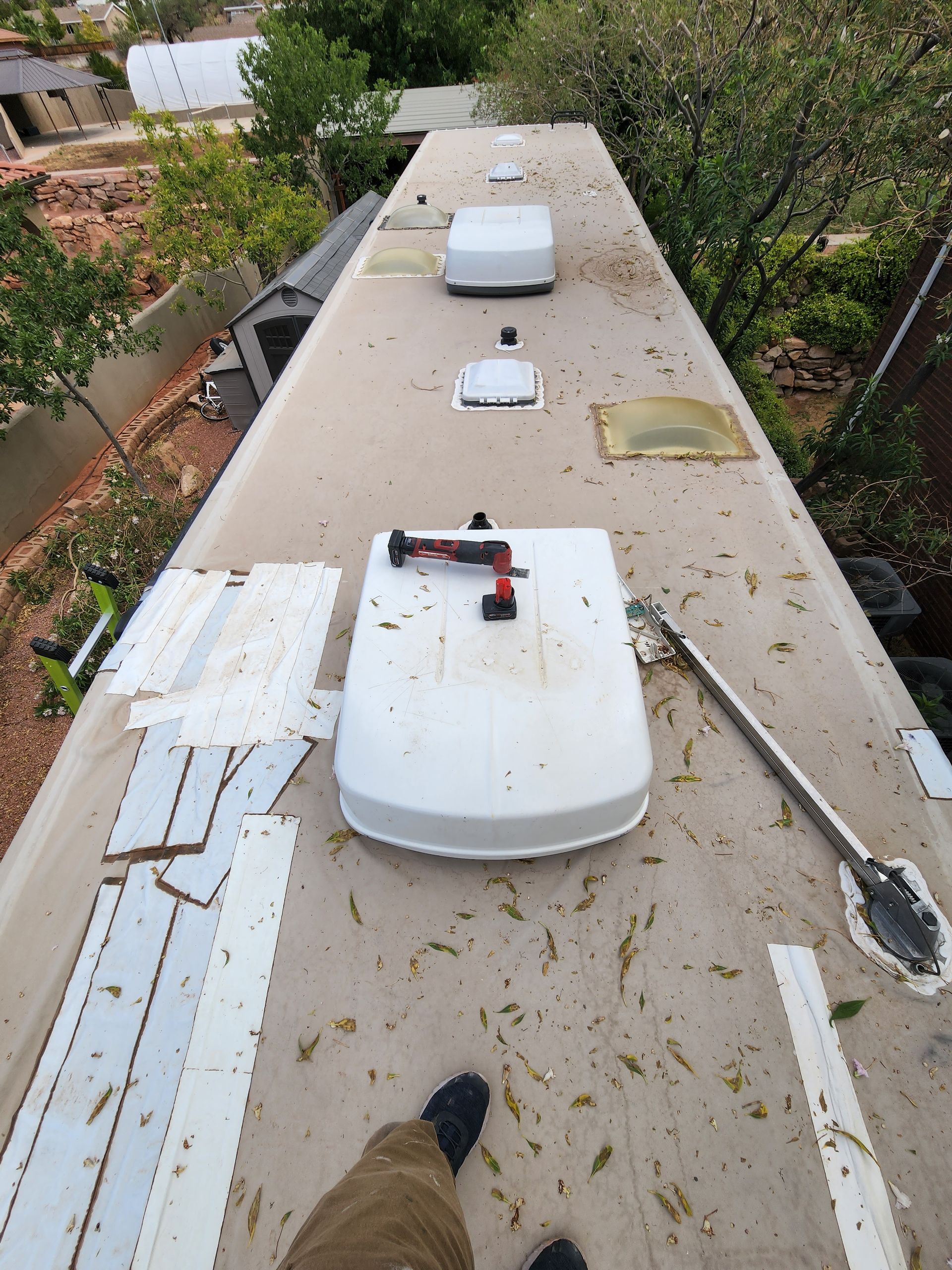 RV roof with AC units, tools, and debris; person standing on it.