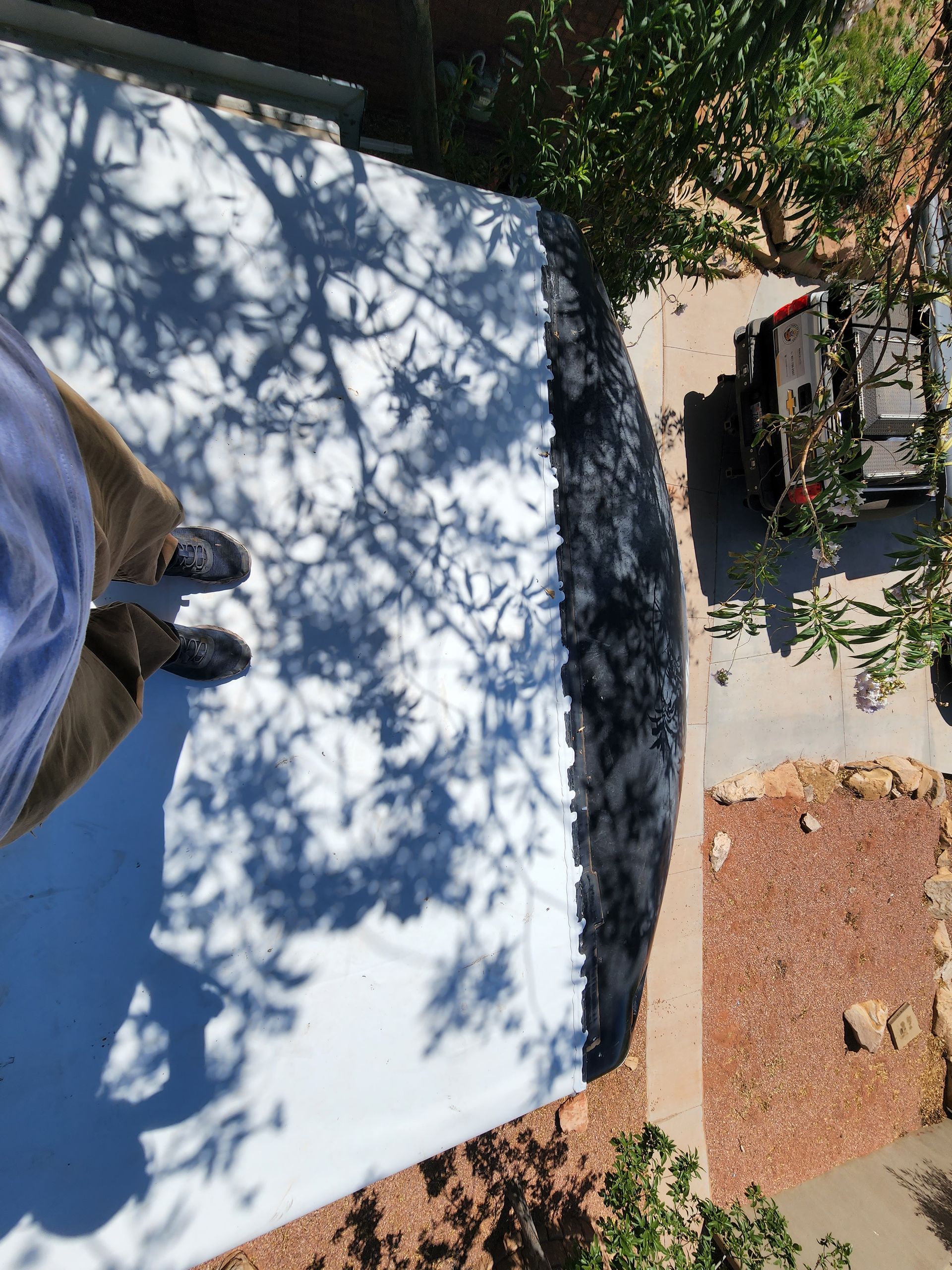 Person standing on a white roof; dark tree shadows. View of a car and ground.