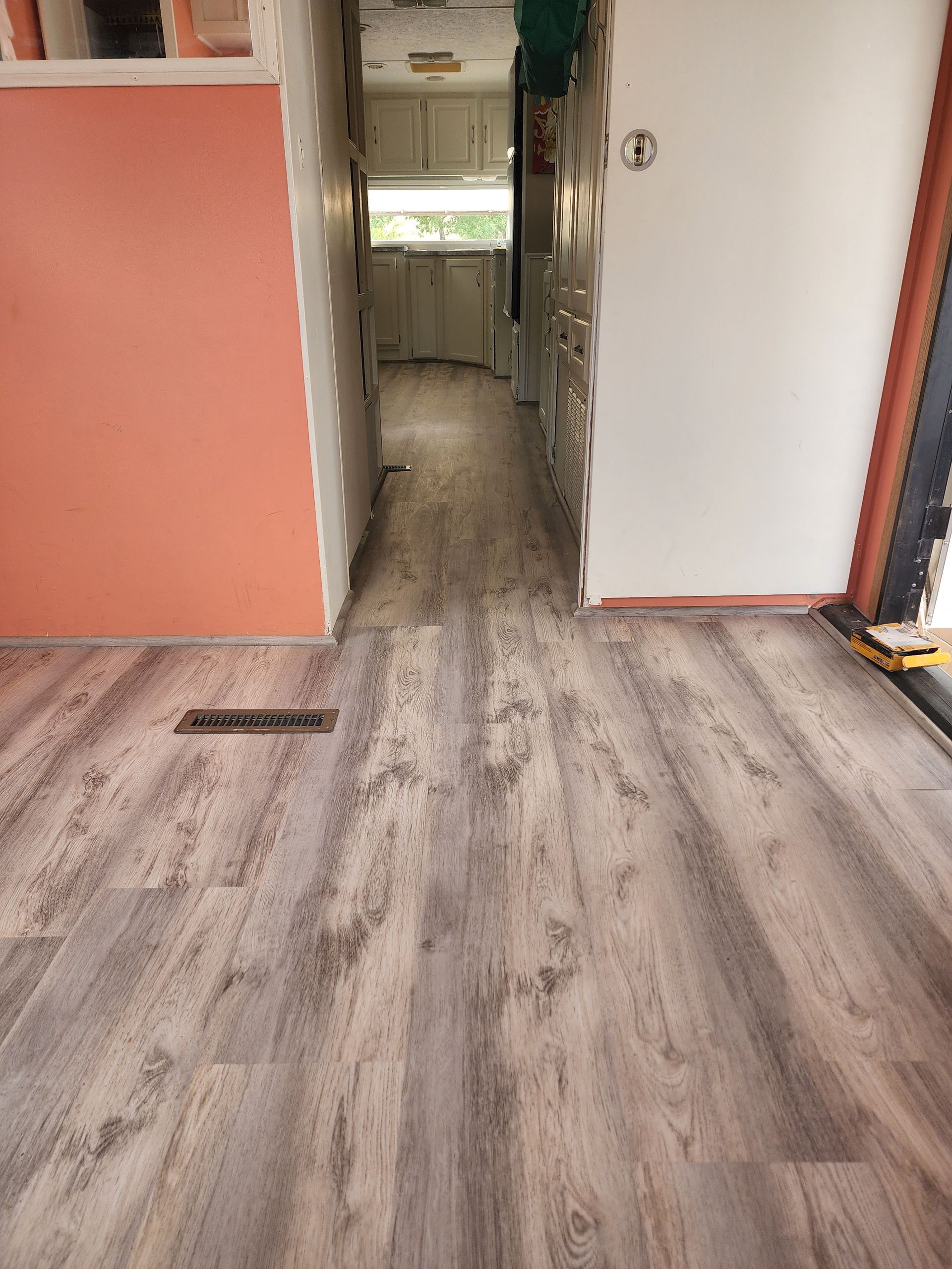 Interior of a mobile home with gray wood-look flooring and a peach-colored wall.