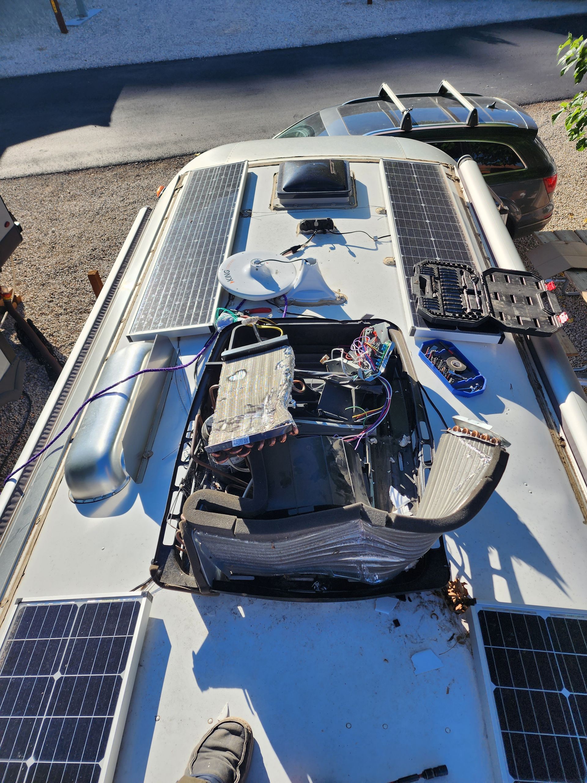 RV roof with damaged vent, solar panels, and a vehicle in the background.
