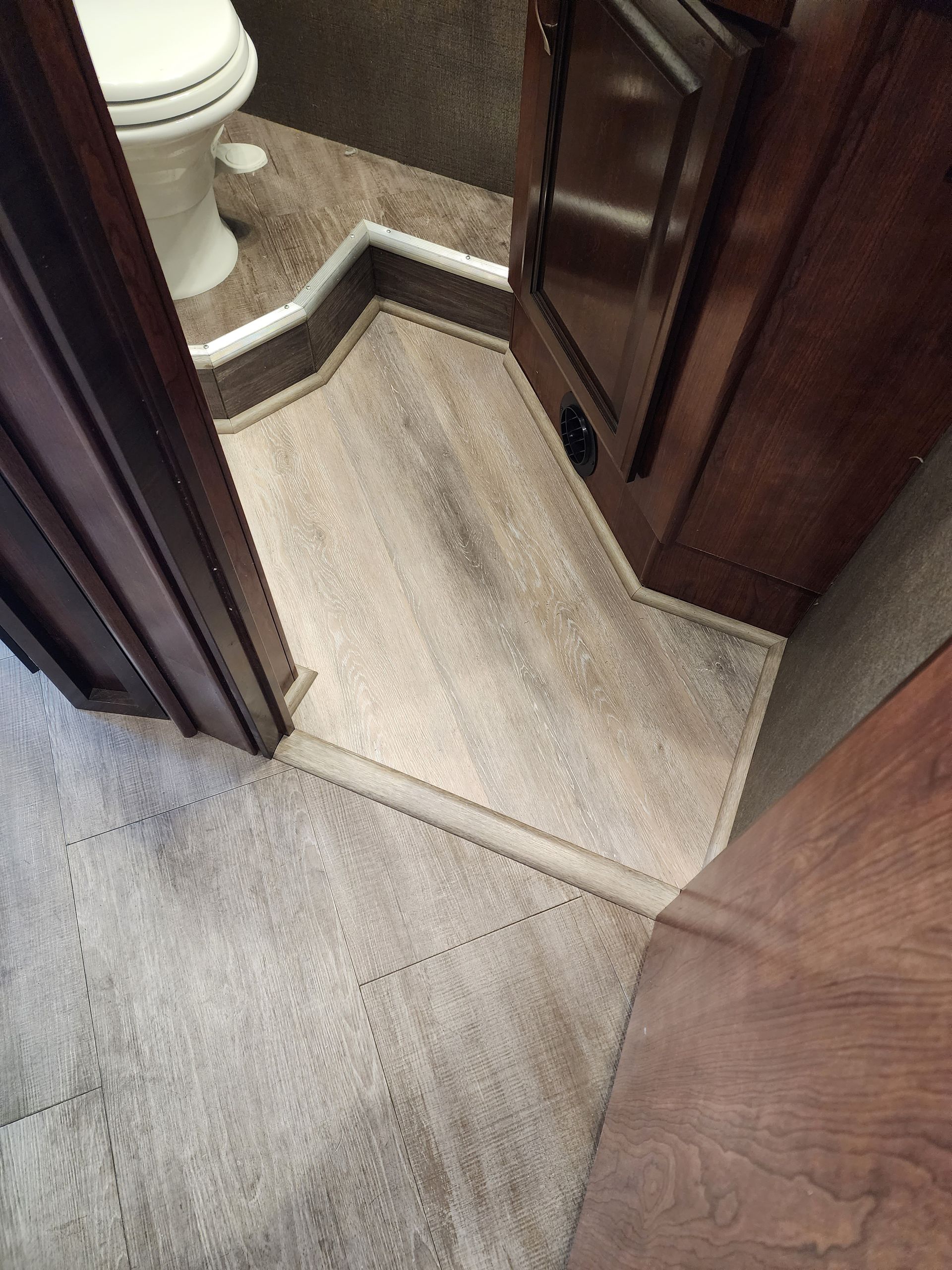 Bathroom with a light brown wood-look floor, adjacent to carpeted area, and brown cabinets.